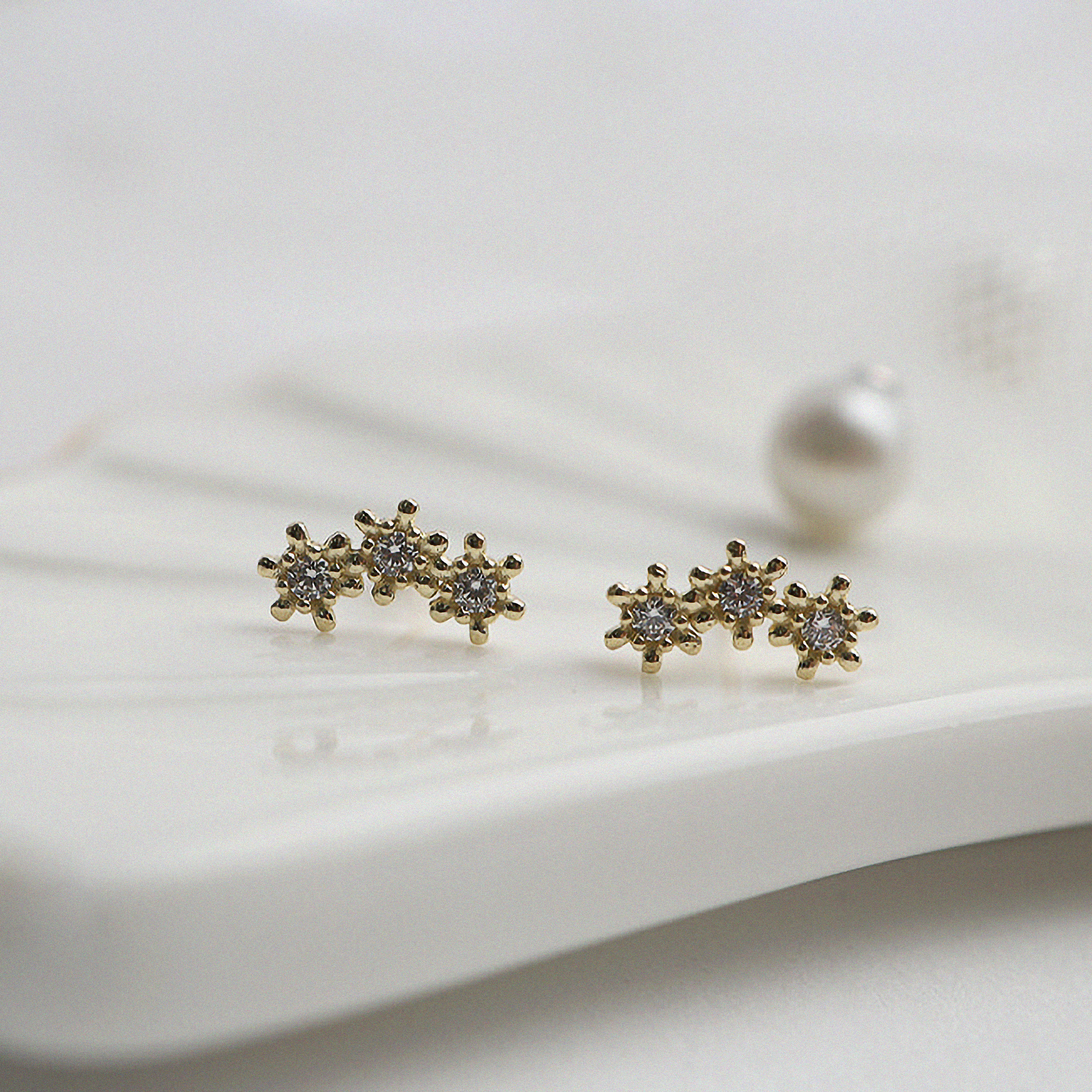 Close up shot of gold earrings featuring three petite cubic zirconia flowers