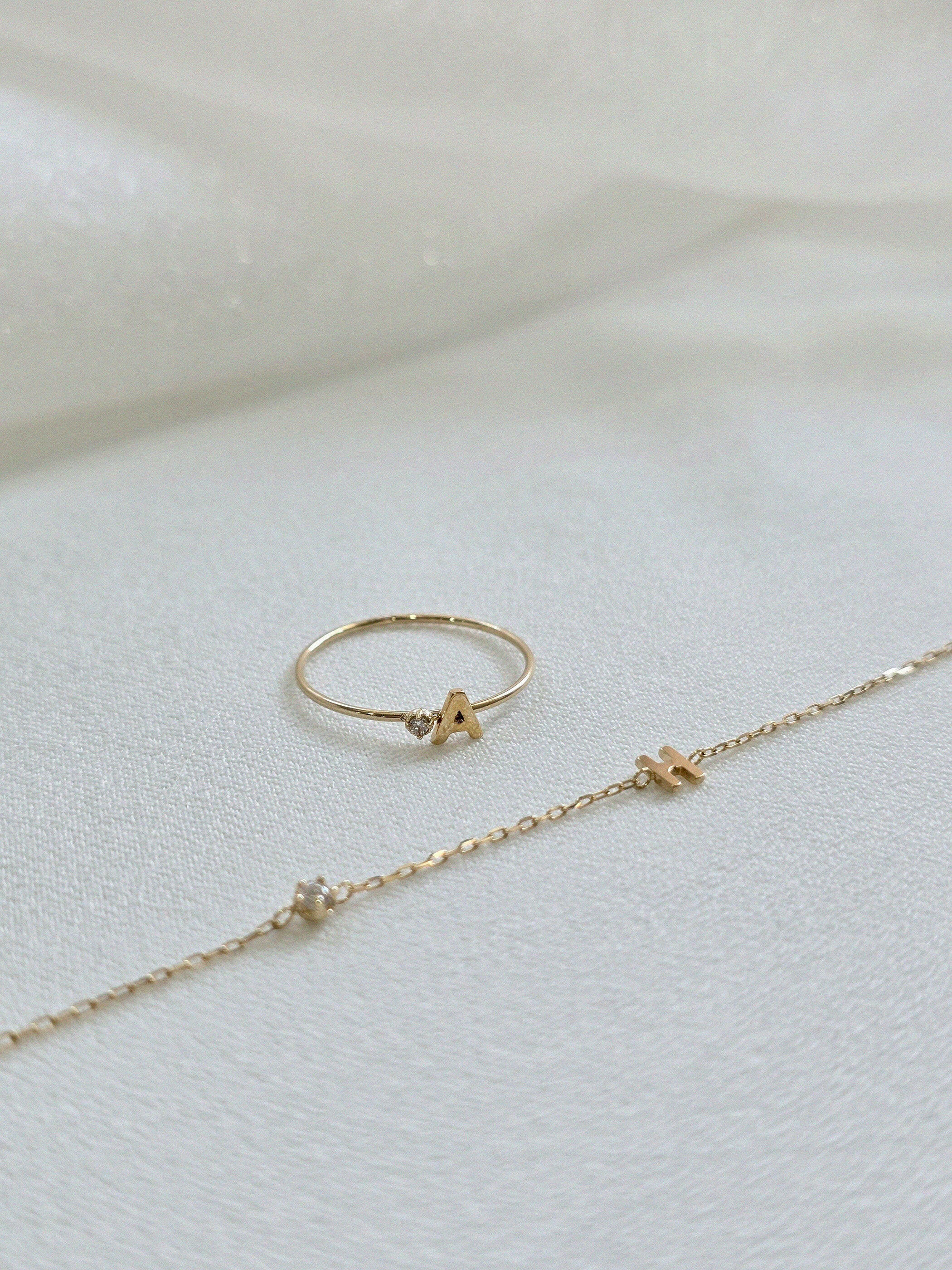 Personalized initial ring presented with initial with diamond bracelet on a soft beigh fabric