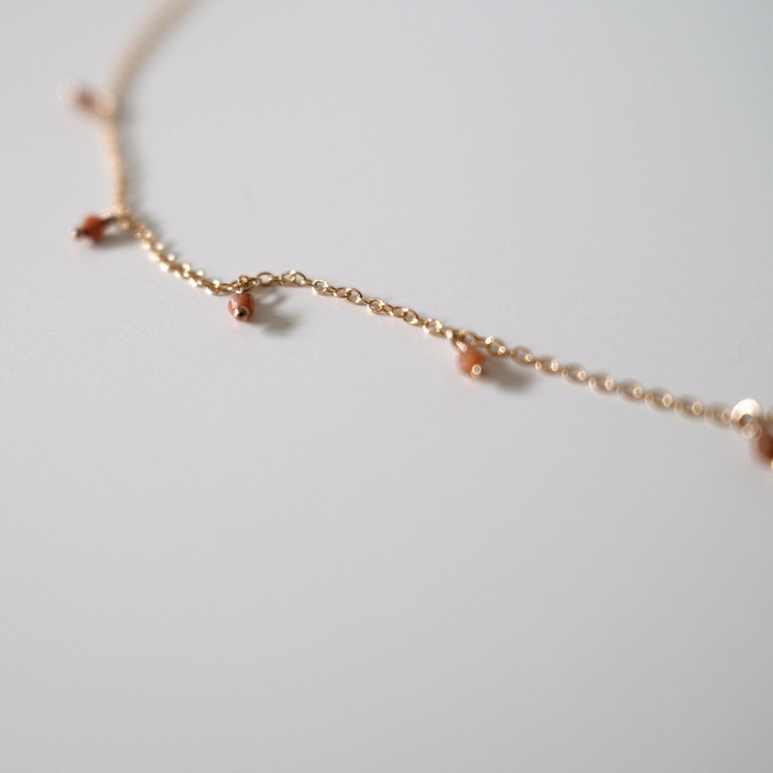 Close-up of minimalist gold chain with tiny dangling brown gemstones