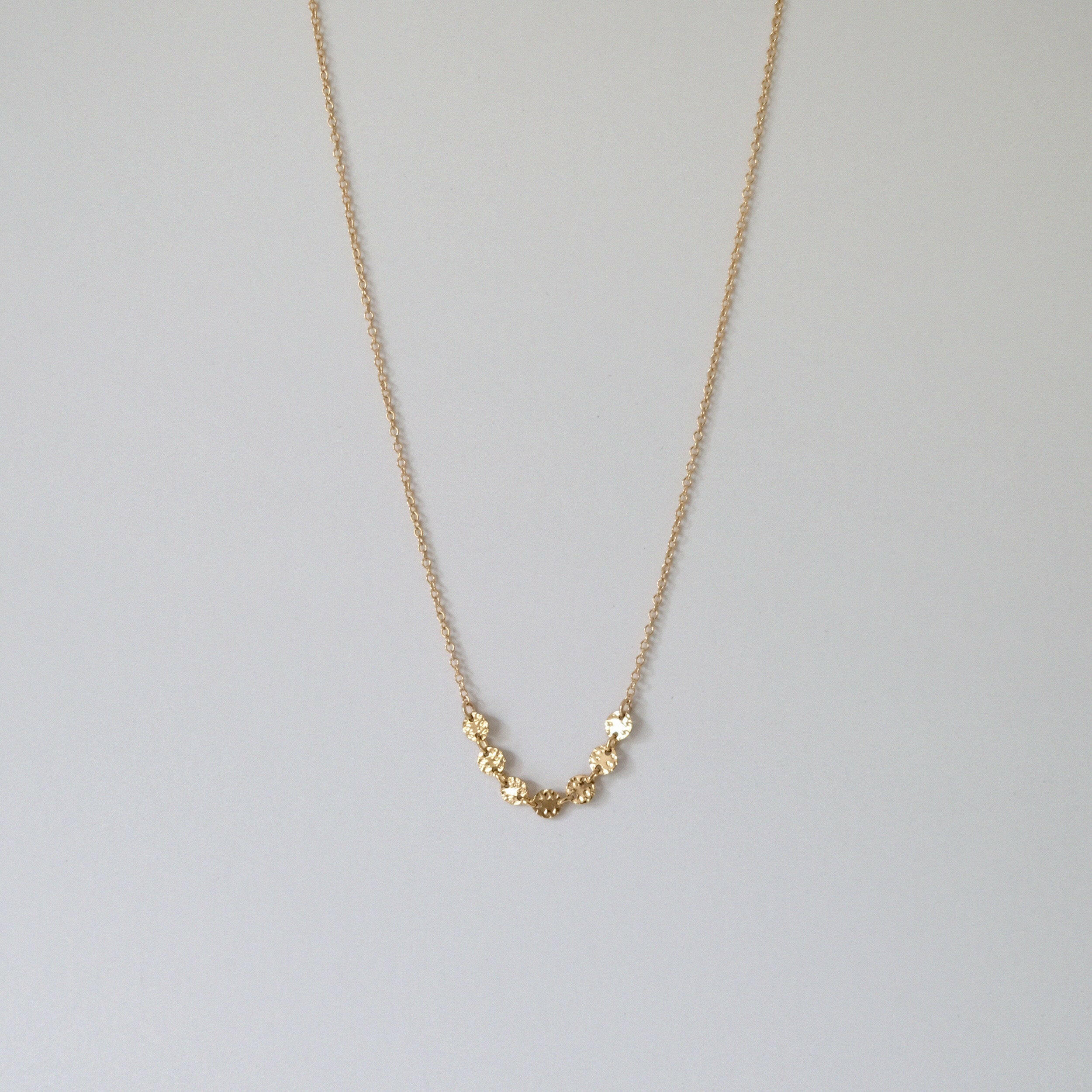 Gold filled necklace with 7 pressed disc charms laid flat