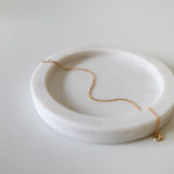 Fine gold bracelet laid on soft beige tray with curved edges