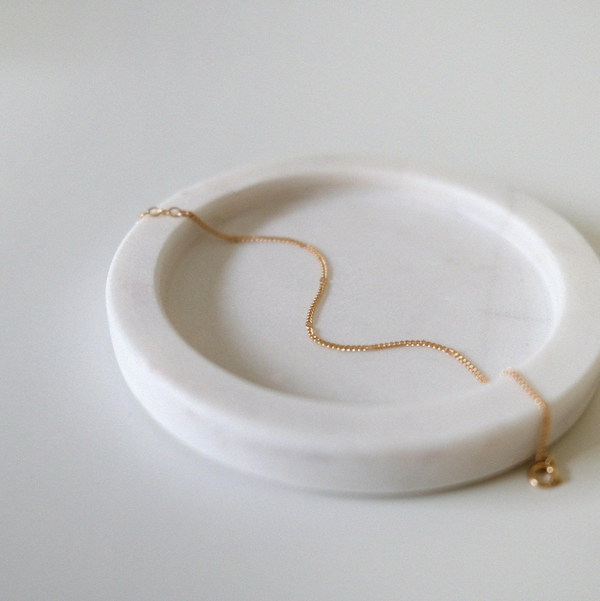 Fine gold bracelet laid on soft beige tray with curved edges