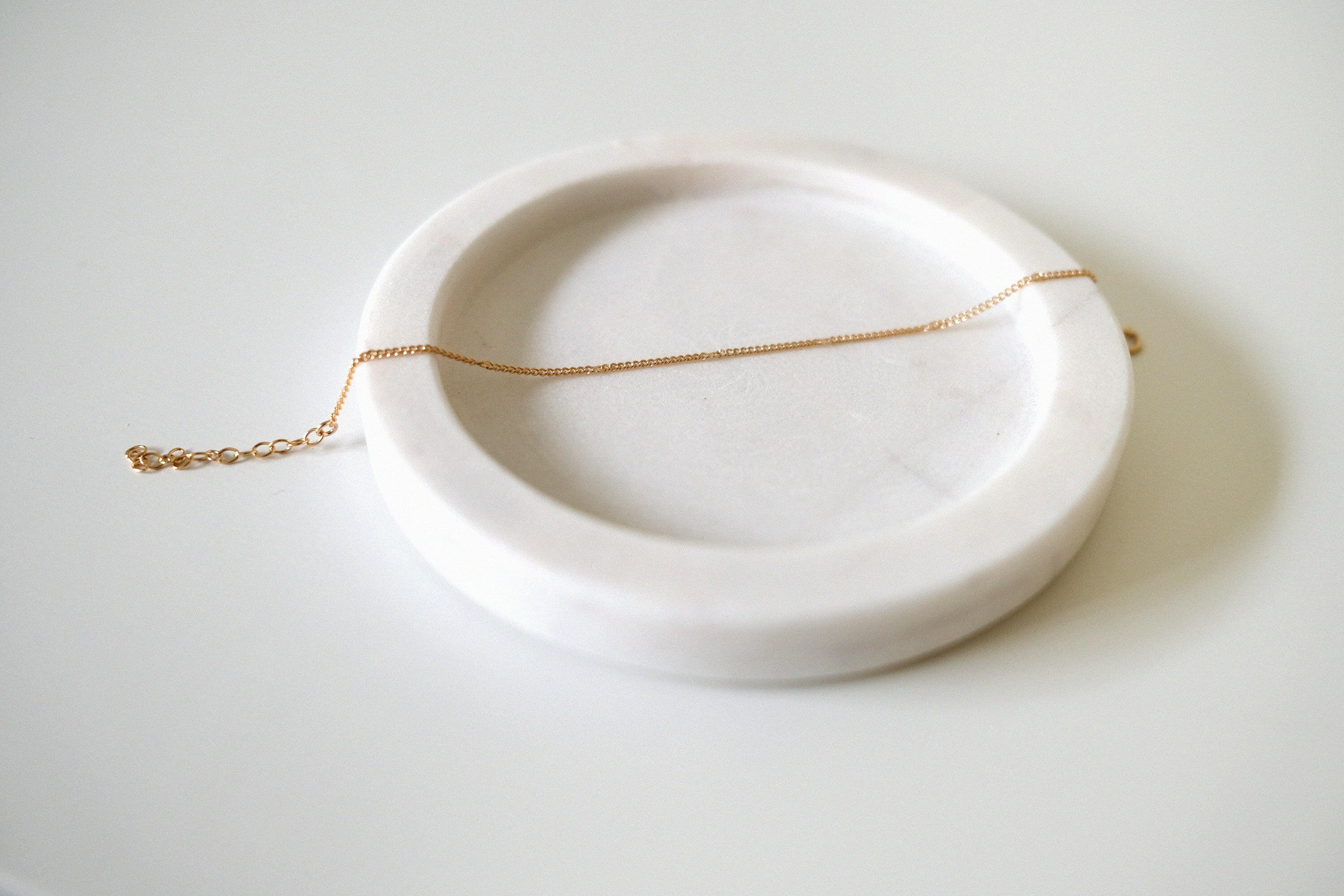 Fine gold bracelet laid on soft beige tray with curved edges