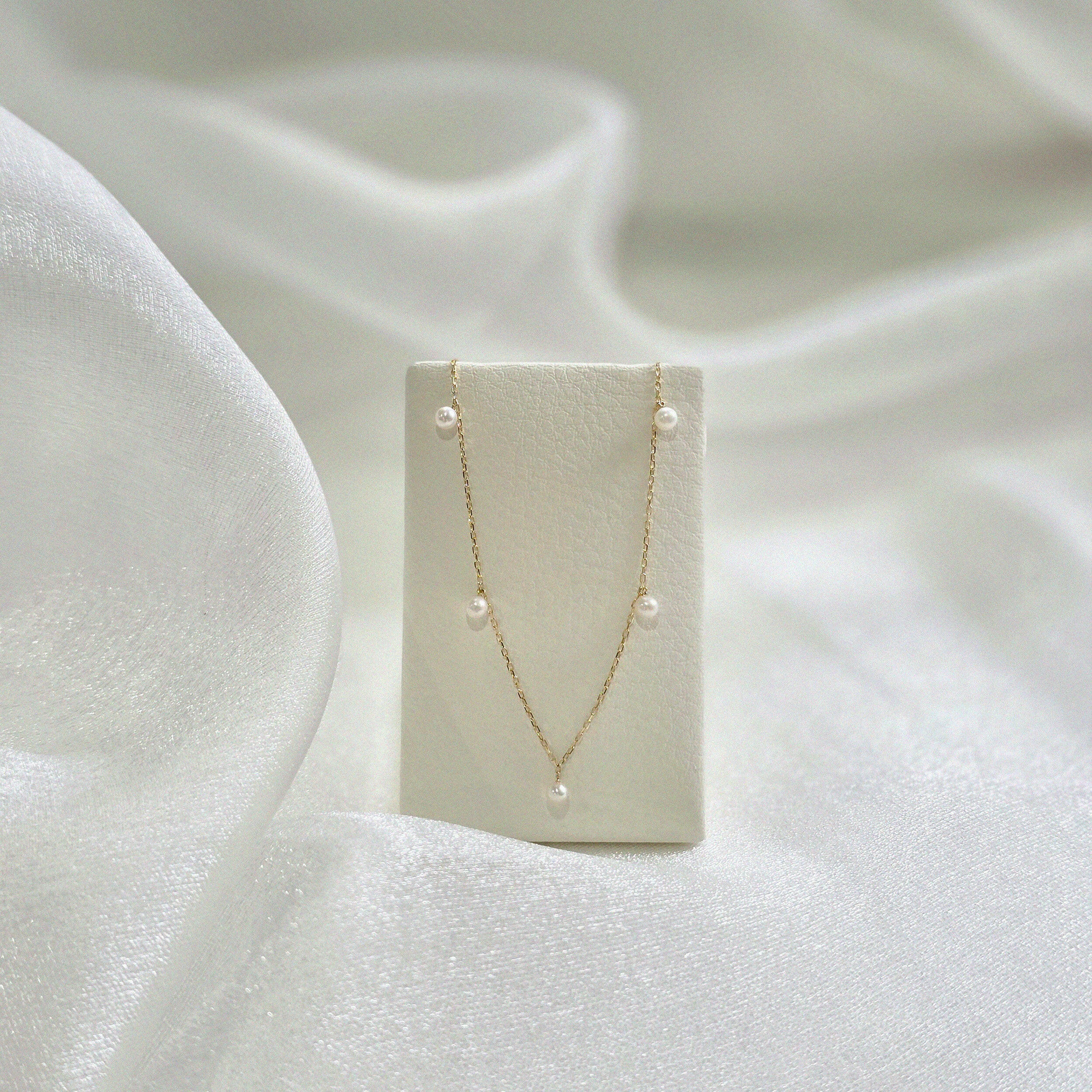 Ariel Perla Necklace displayed on cream leather necklace stand, pearls symmetrically aligned