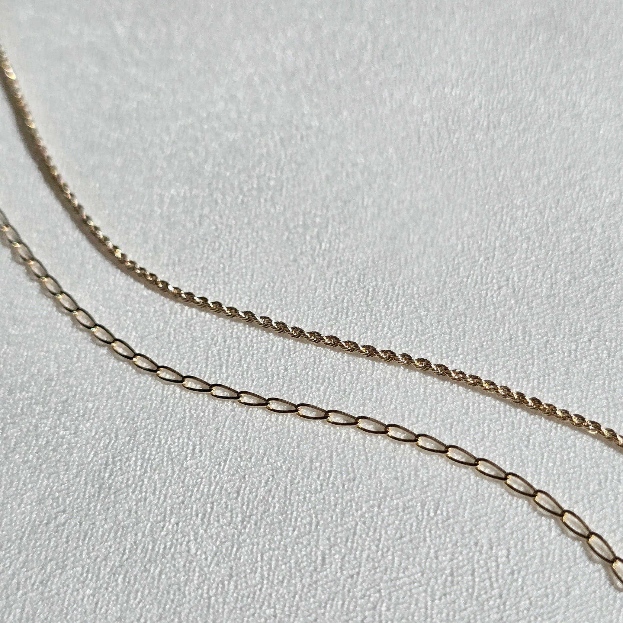 Twisted rope bracelet and other gold chain bracelet presented on textured neutral display fabric