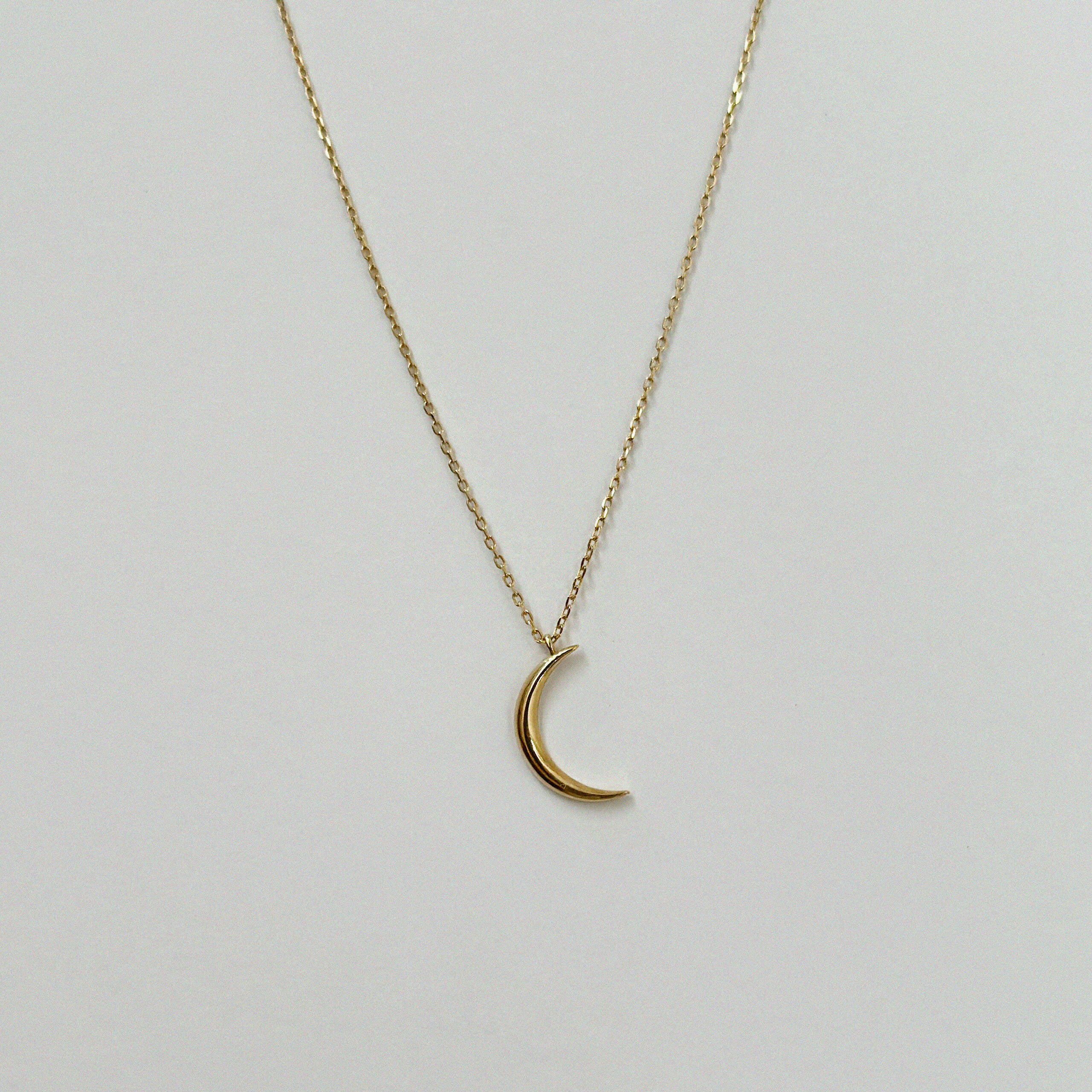 Close-up of 14mm crescent moon pendant in high-polish 14K gold, symbolizing femininity and intuition