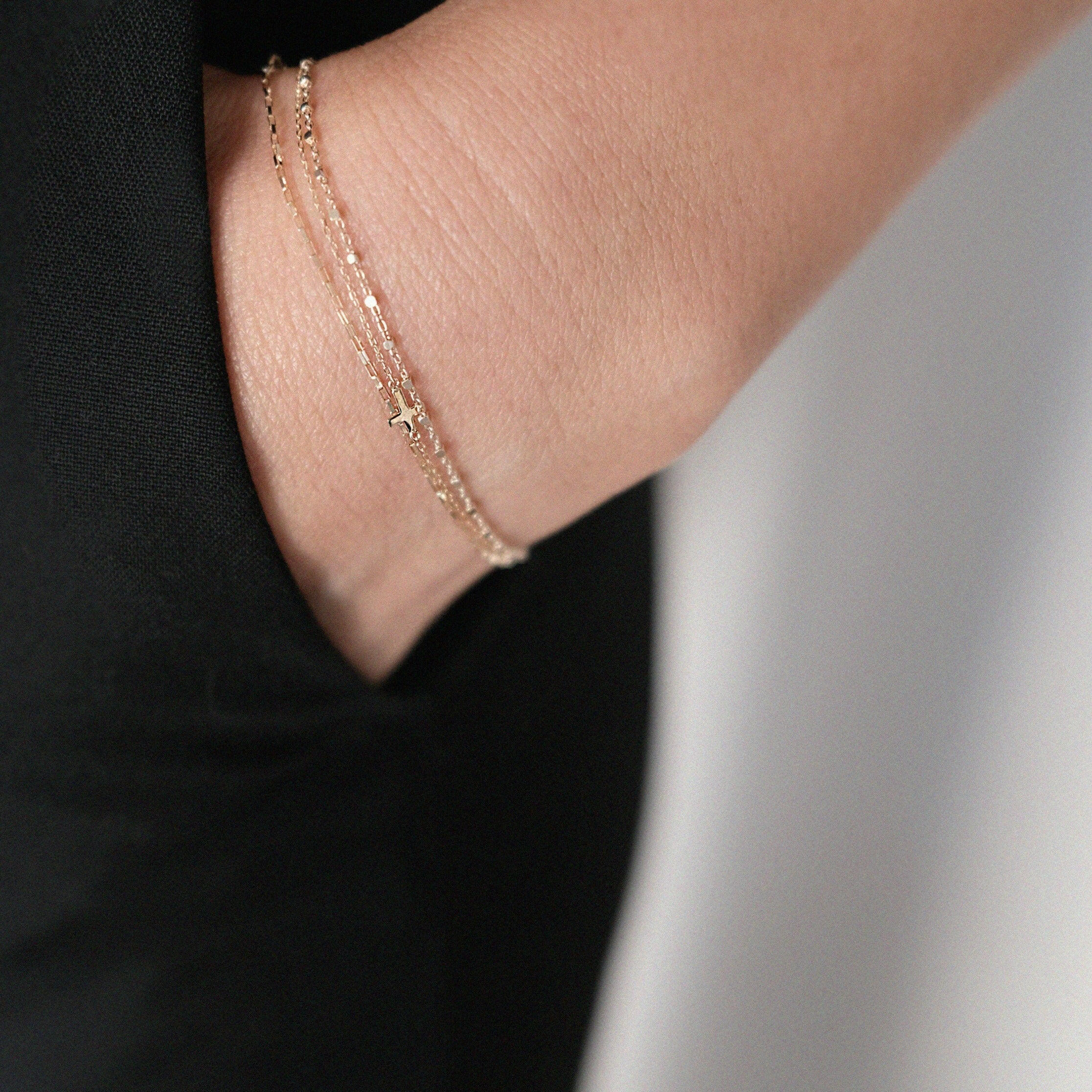 14K Petite Cross Bracelet layered on wrist for a refined look, paired with classic black clothing