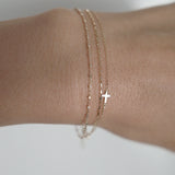 Model wearing the Petite Cross Bracelet layered with dainty gold chains for a delicate, stacked look
