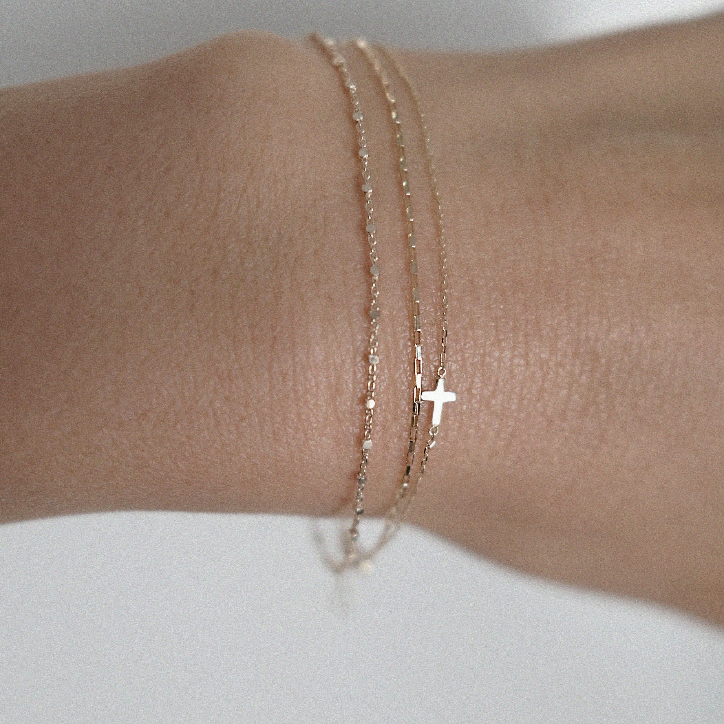 Model wearing the Petite Cross Bracelet layered with dainty gold chains for a delicate, stacked look