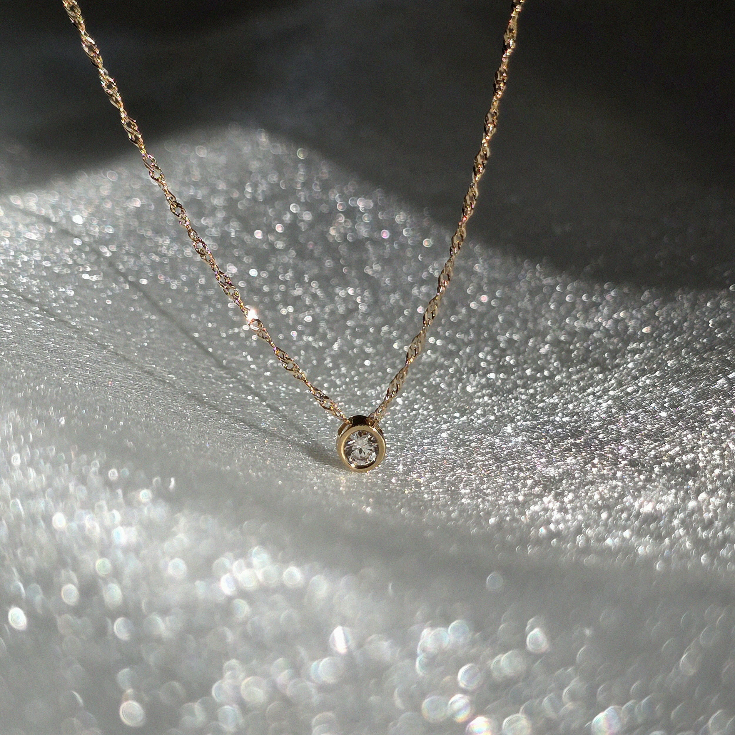 Close-up of cubic zirconia pendant on 14K solid gold necklace, capturing light reflections on the stone and chain links
