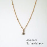 Gold filled necklace with cubic zirconia pendant and dot accents laid flat