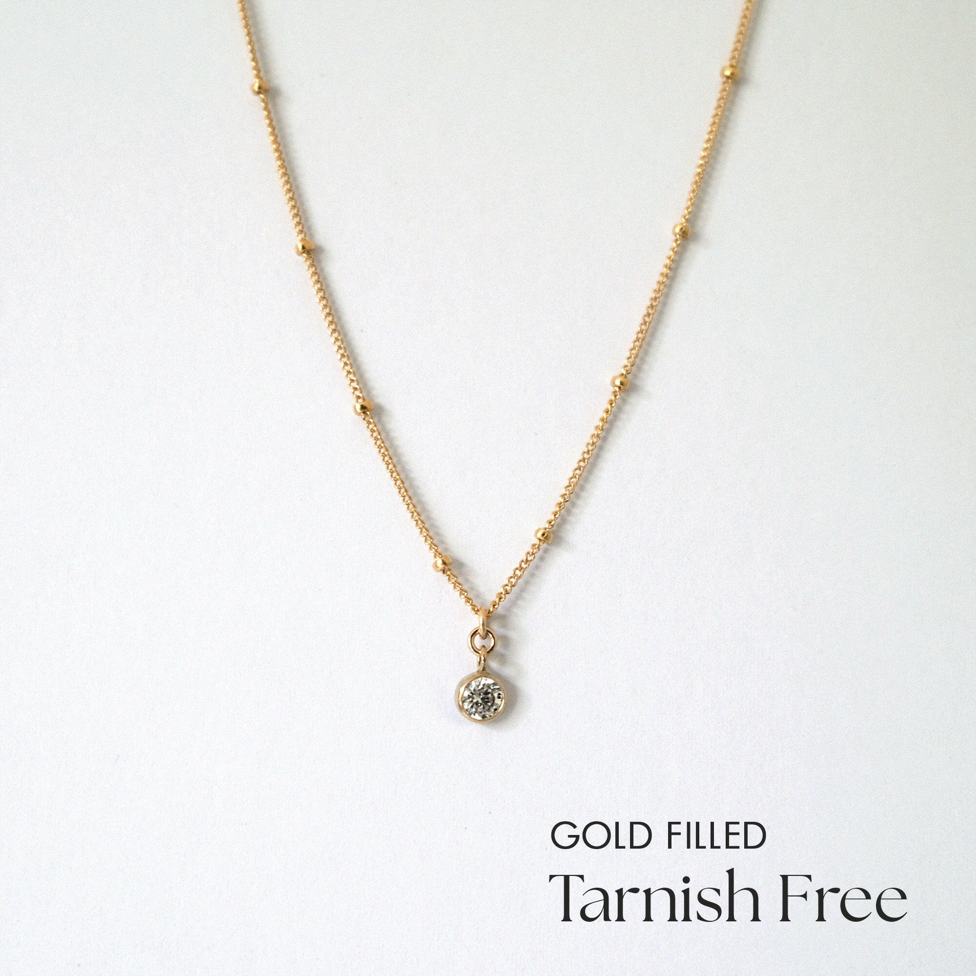 Gold filled necklace with cubic zirconia pendant and dot accents laid flat