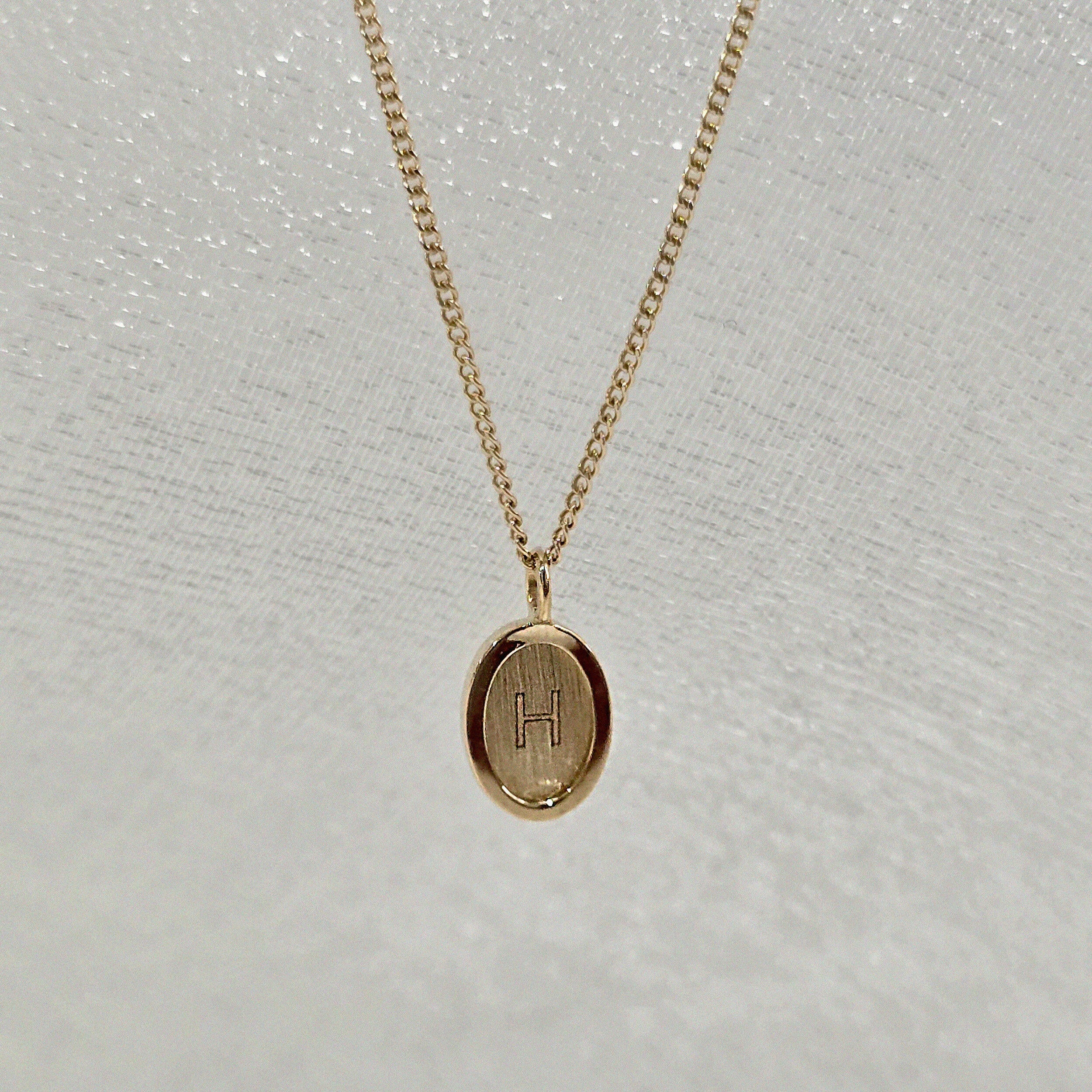 Close-up of the engraved oval initial pendant in solid 14K gold