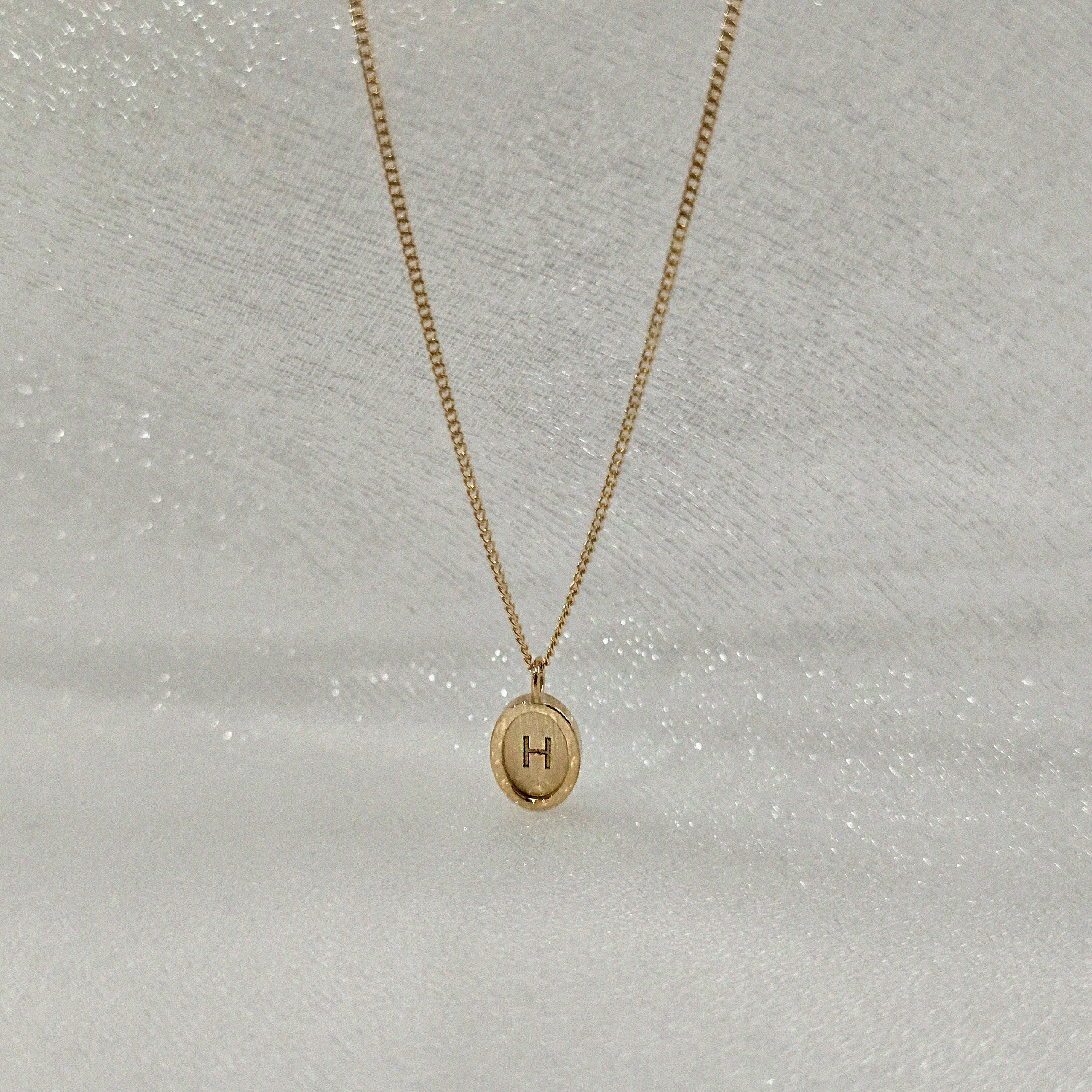 Extreme close-up of 14K solid gold Dear Initial oval pendant engraved with custom letter – high polish finish and delicate texture