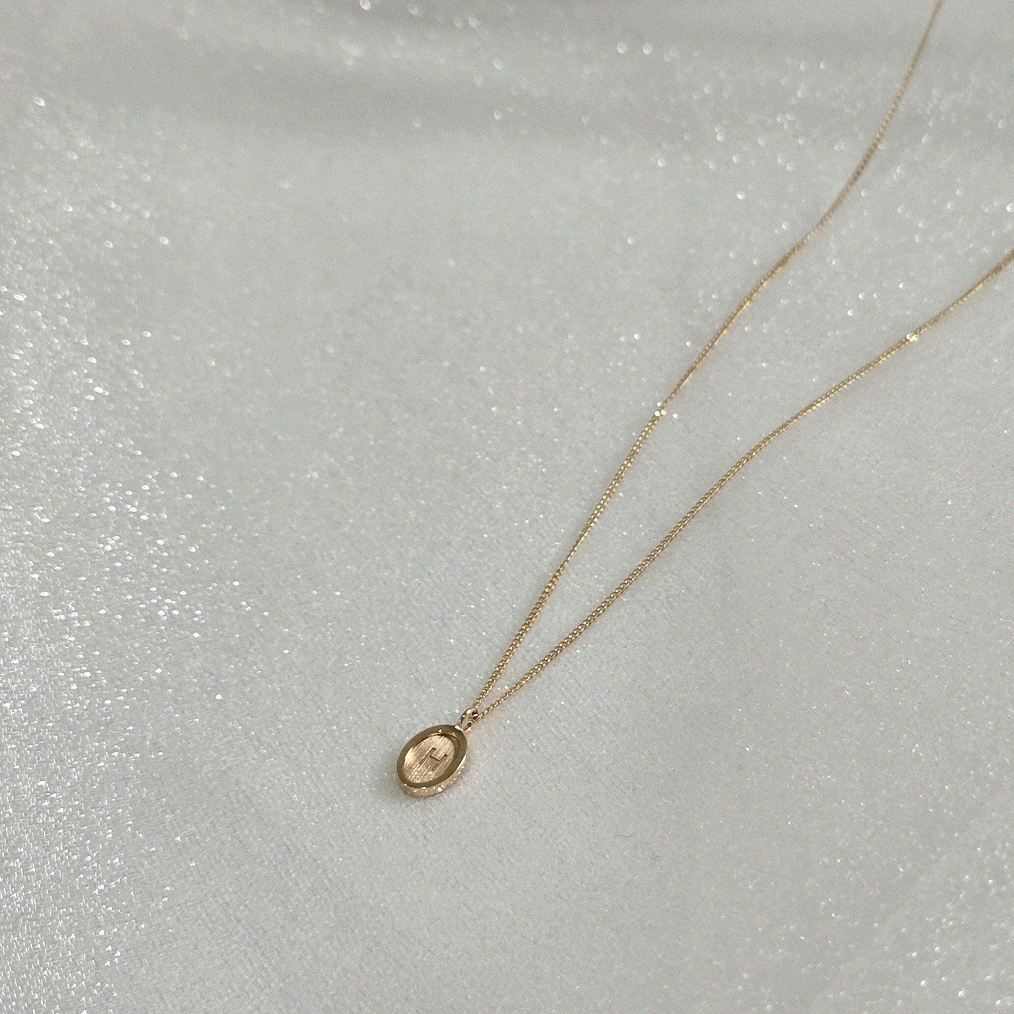 Side angle of oval initial pendant showing curvature and thickness – suspended on a dainty 14K gold chain
