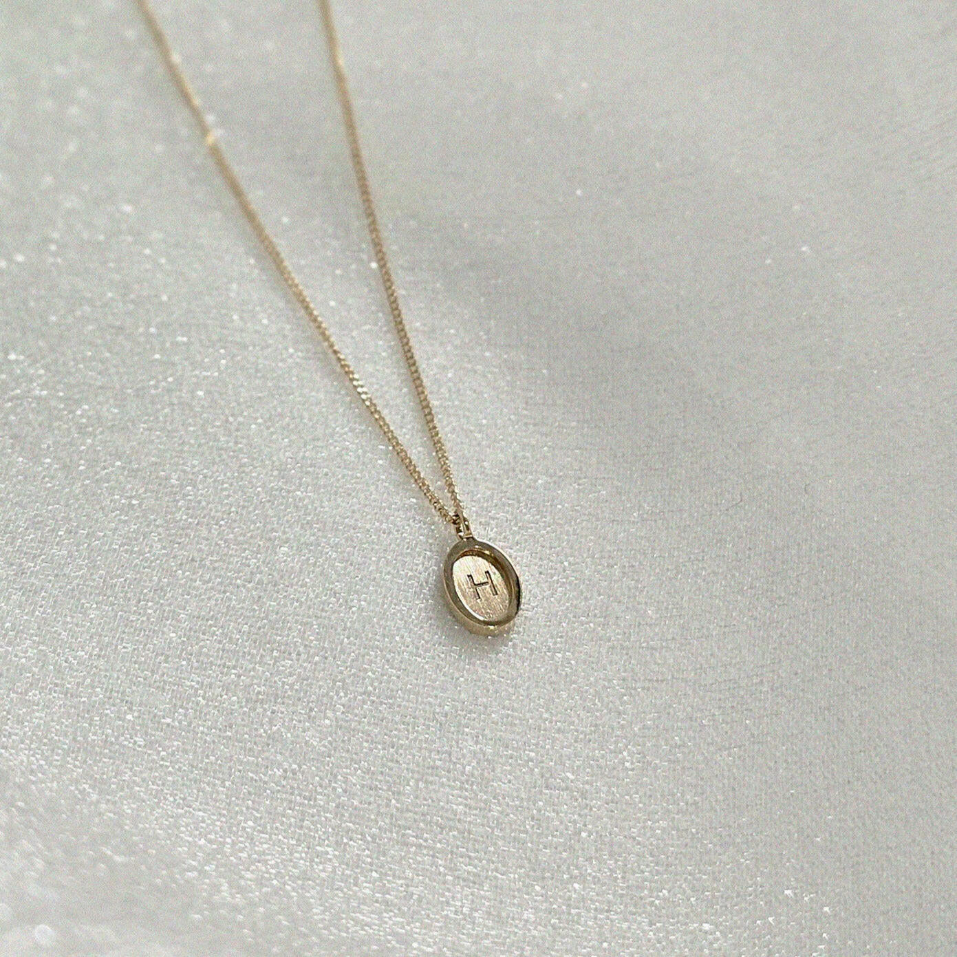 Overhead view of the oval 14K gold initial charm on chain – handcrafted and reflective under light