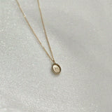 Overhead view of the oval 14K gold initial charm on chain – handcrafted and reflective under light