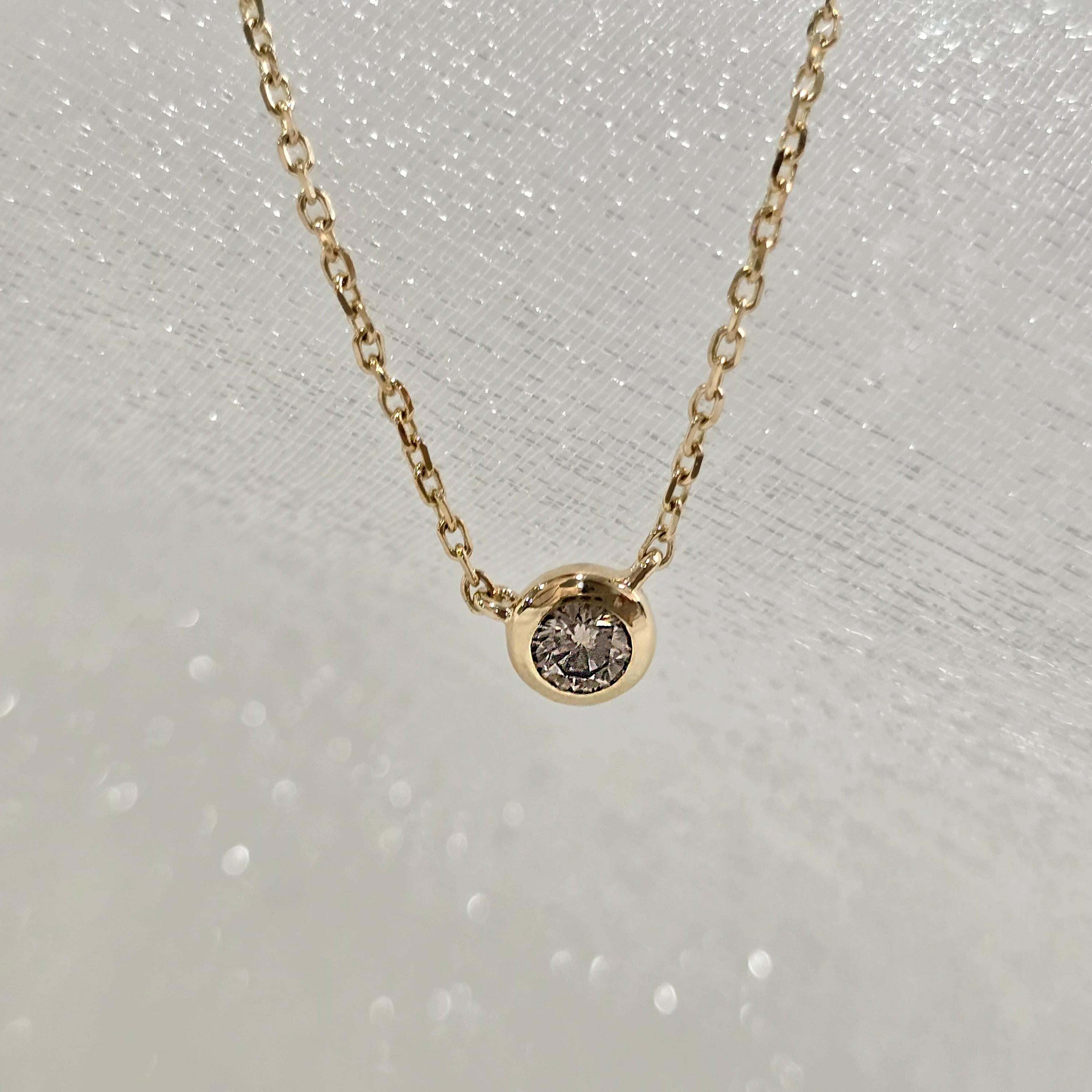 Overhead view of single round diamond set in a minimal 14K gold bezel pendant
