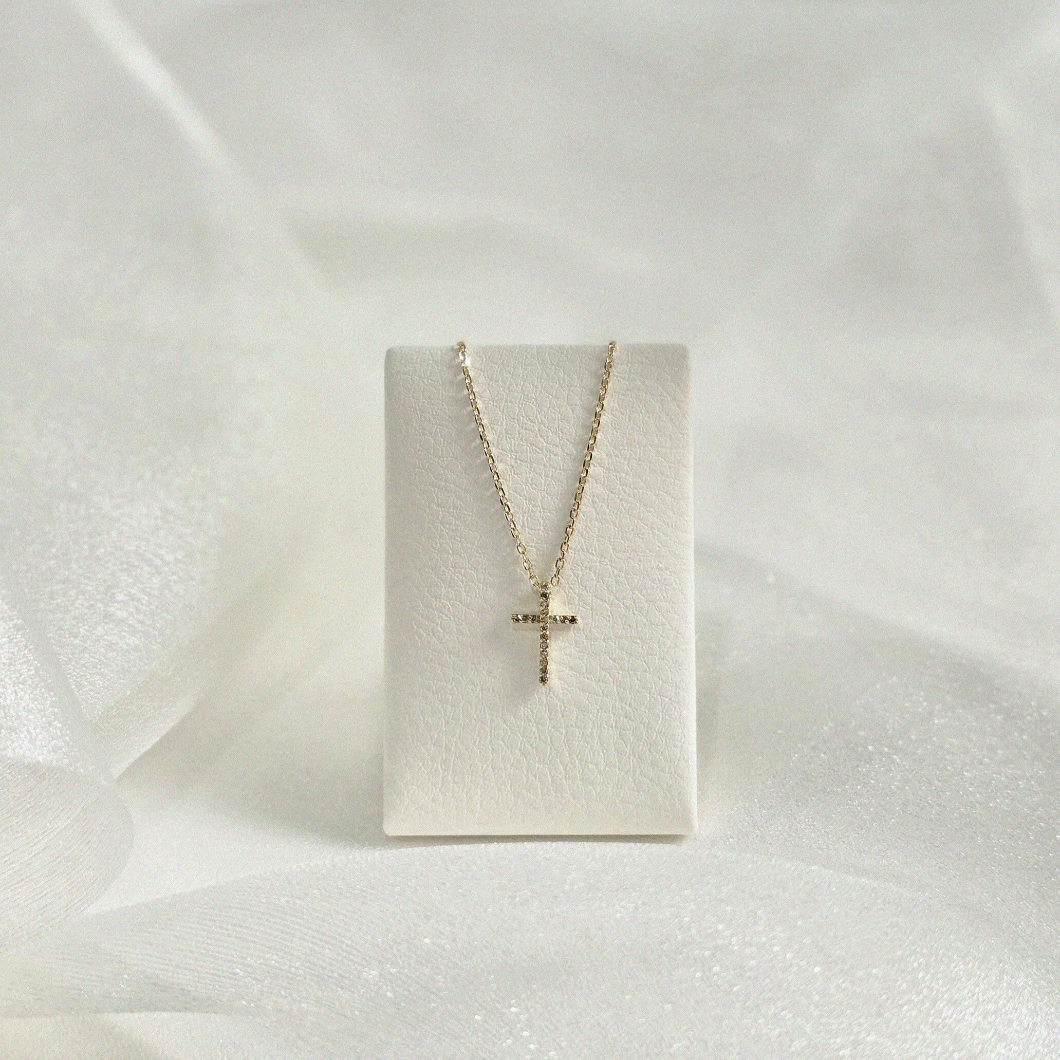 Diamond cross necklace on soft cream leather necklace stand, pendant in focus