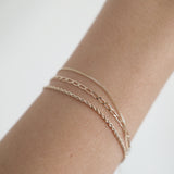 Close-up of slim link bracelet layered with other gold pieces