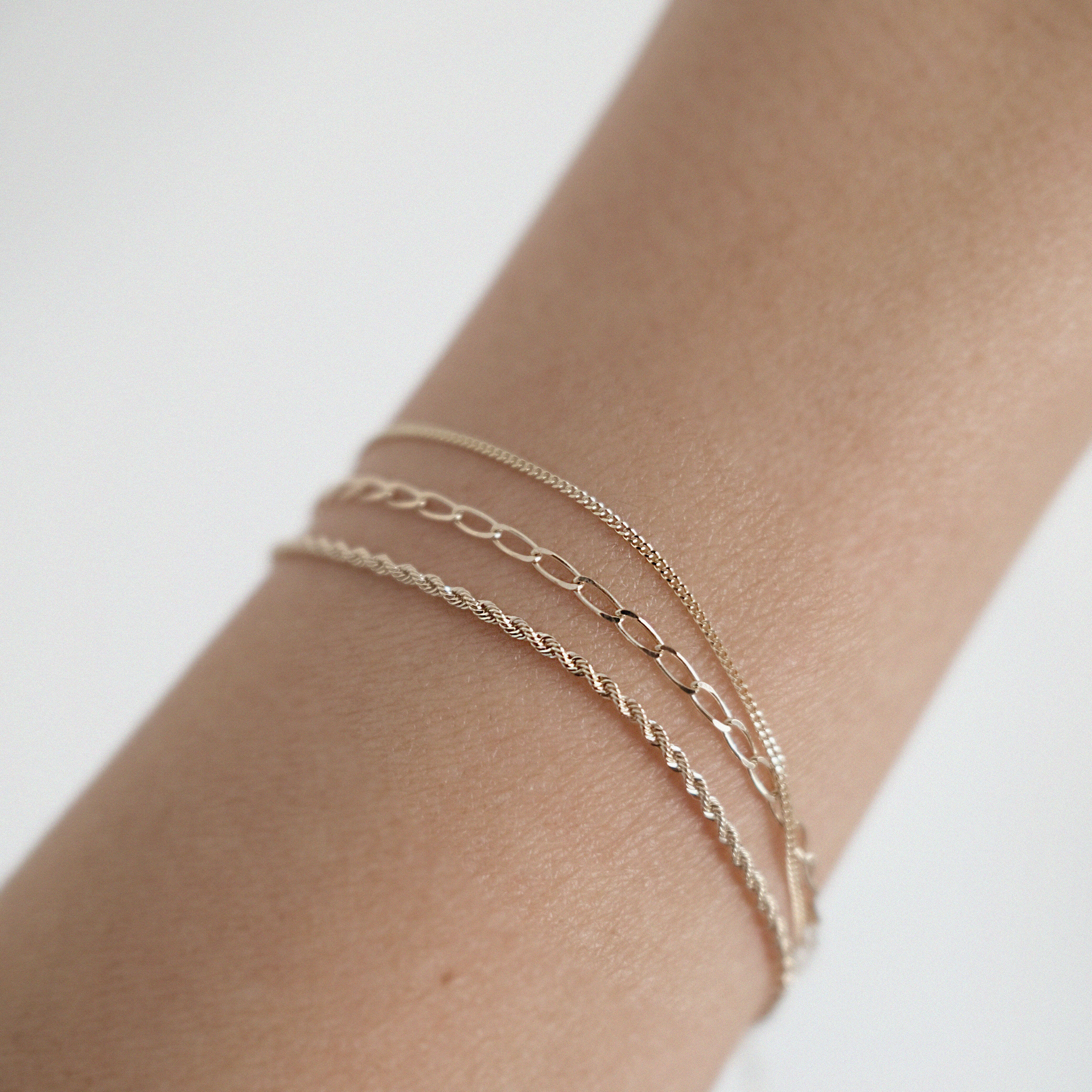 Close-up of slim link bracelet layered with other gold pieces