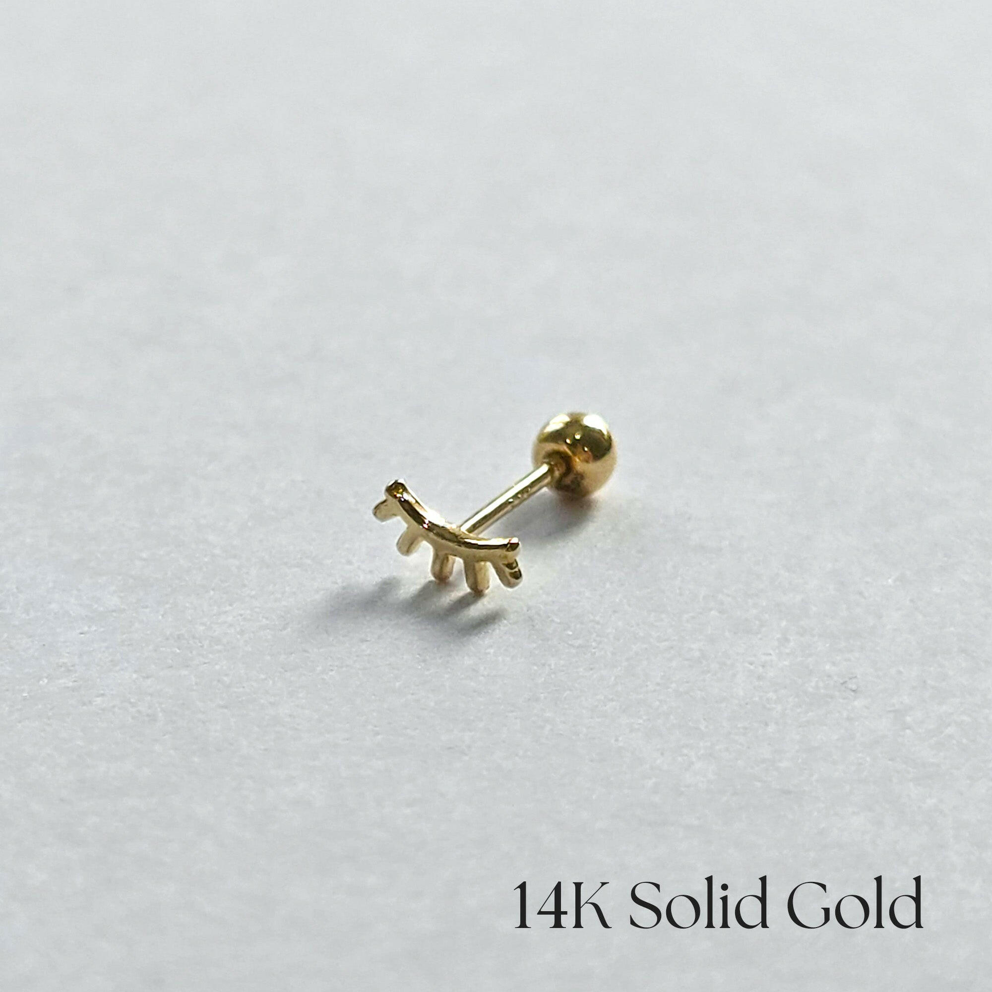 Playful lash-shaped stud in solid gold shown from side angle on white background