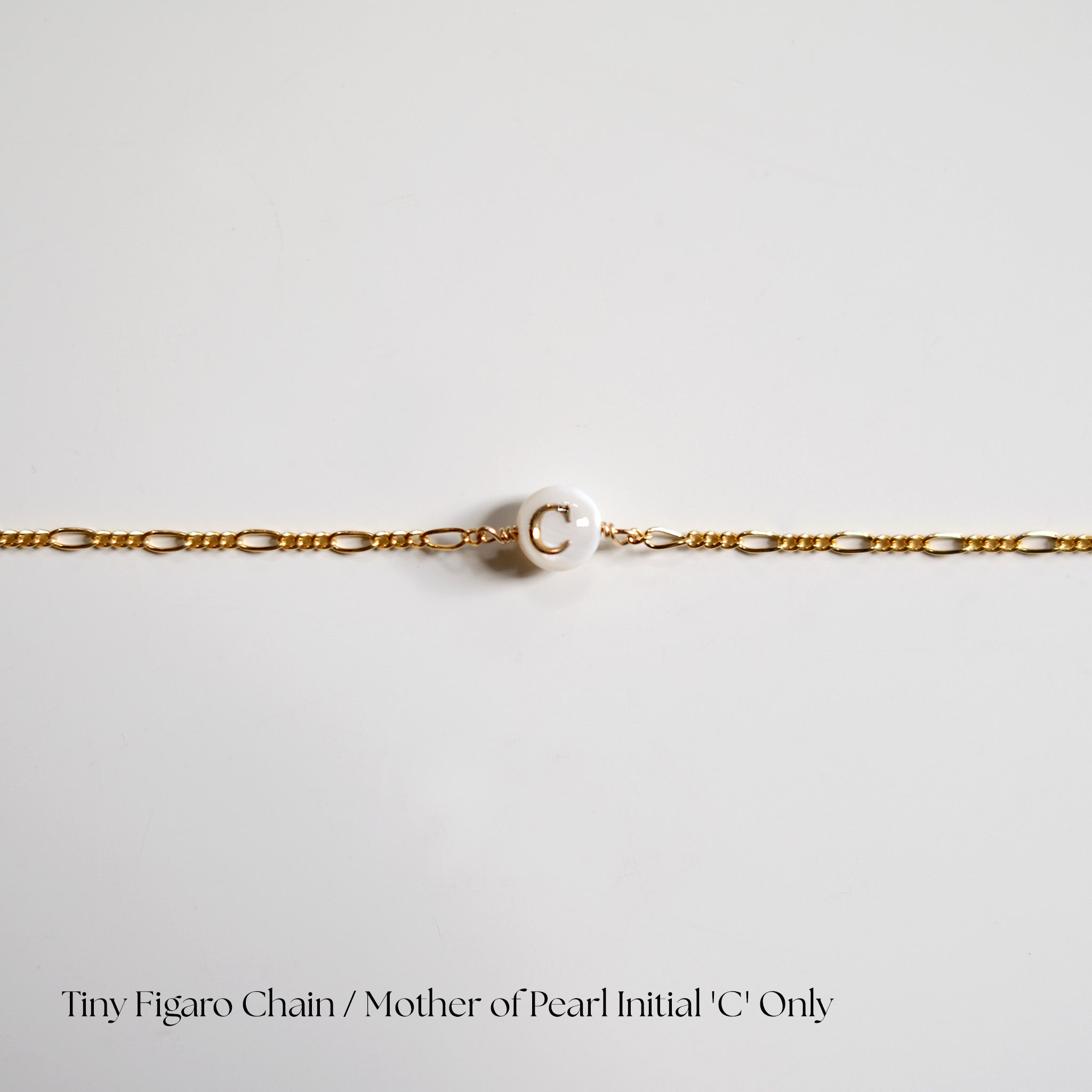 Gold chain with a pearl initial 'C' on a light gray background