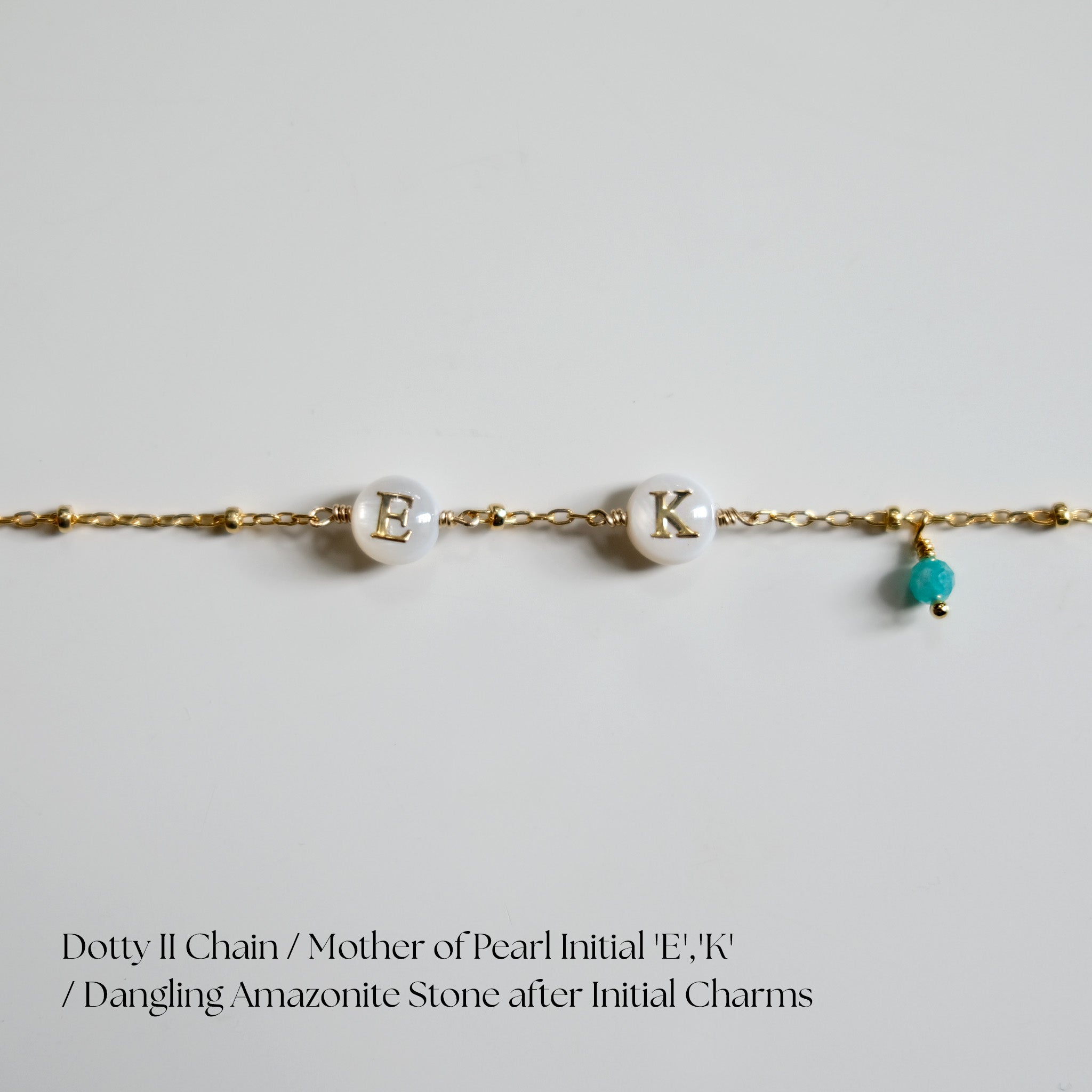 Gold chain bracelet with 'E', 'K' charms and a dangling Amazonite stone on a light gray background.