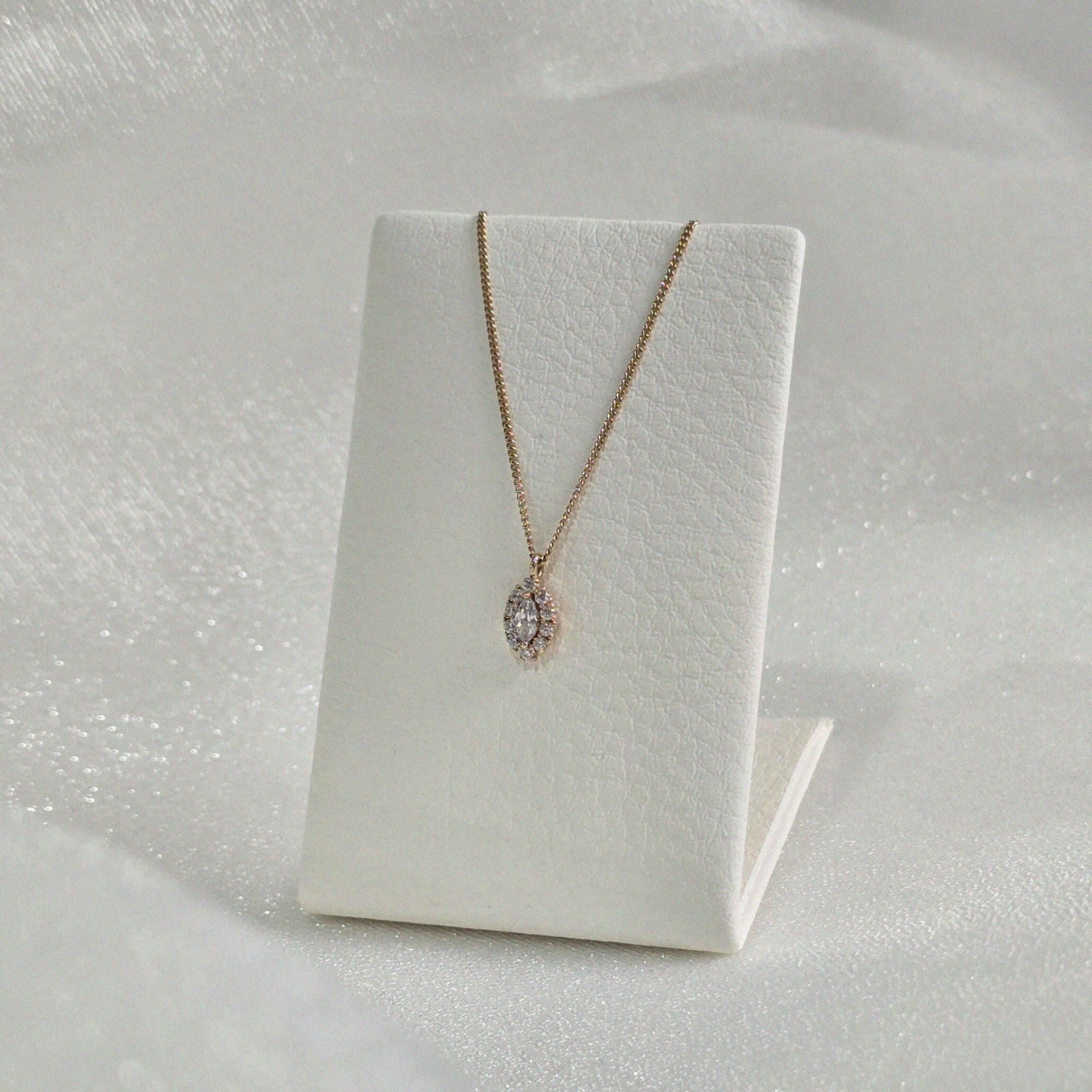 14K Solid Gold Gleam Necklace styled on a minimal necklace stand with soft lighting