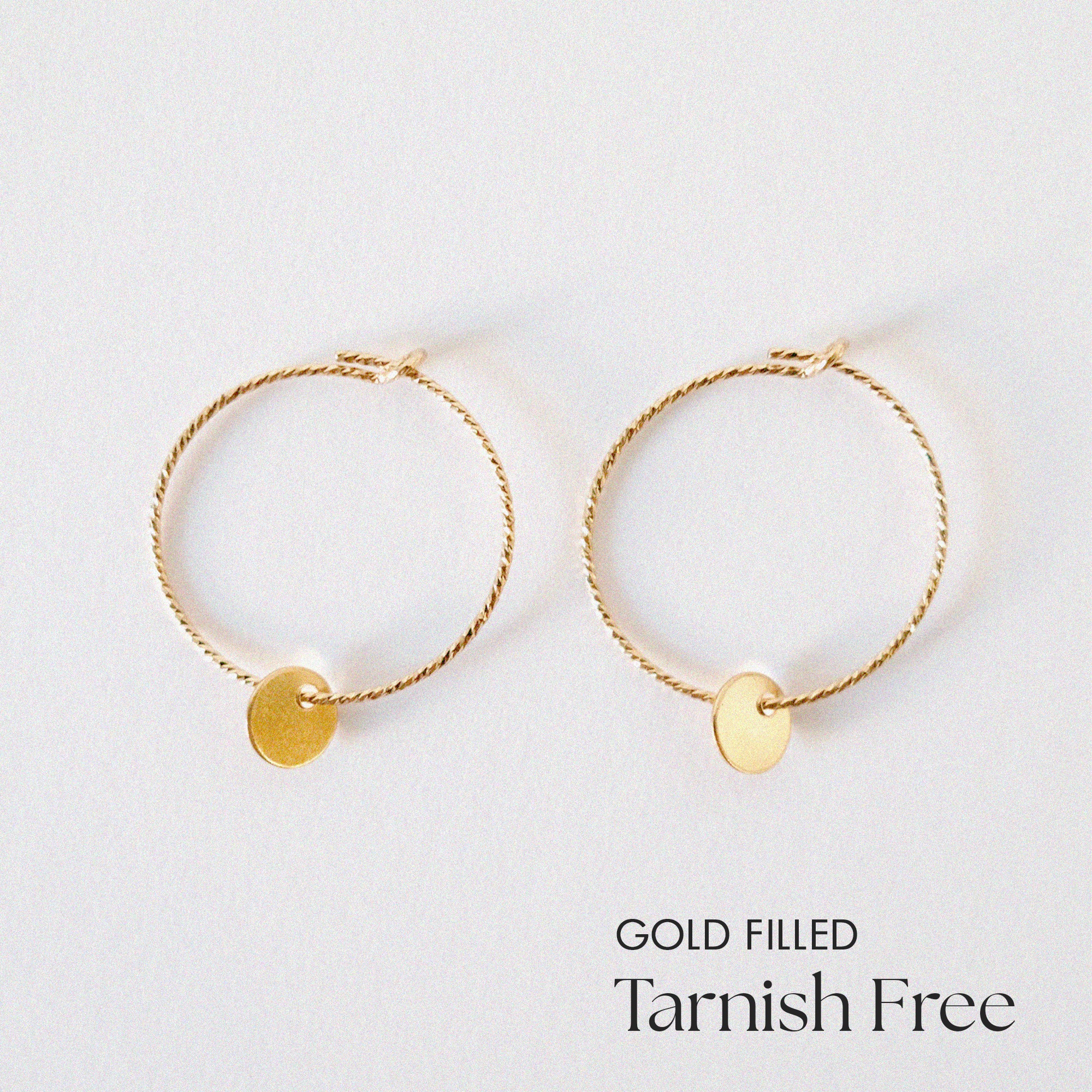 Gold-filled Aster hoop earrings with 5mm disc accent laid flat on a white background