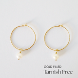 Gold-filled hoop earrings with freshwater pearl accent laid flat on white surface