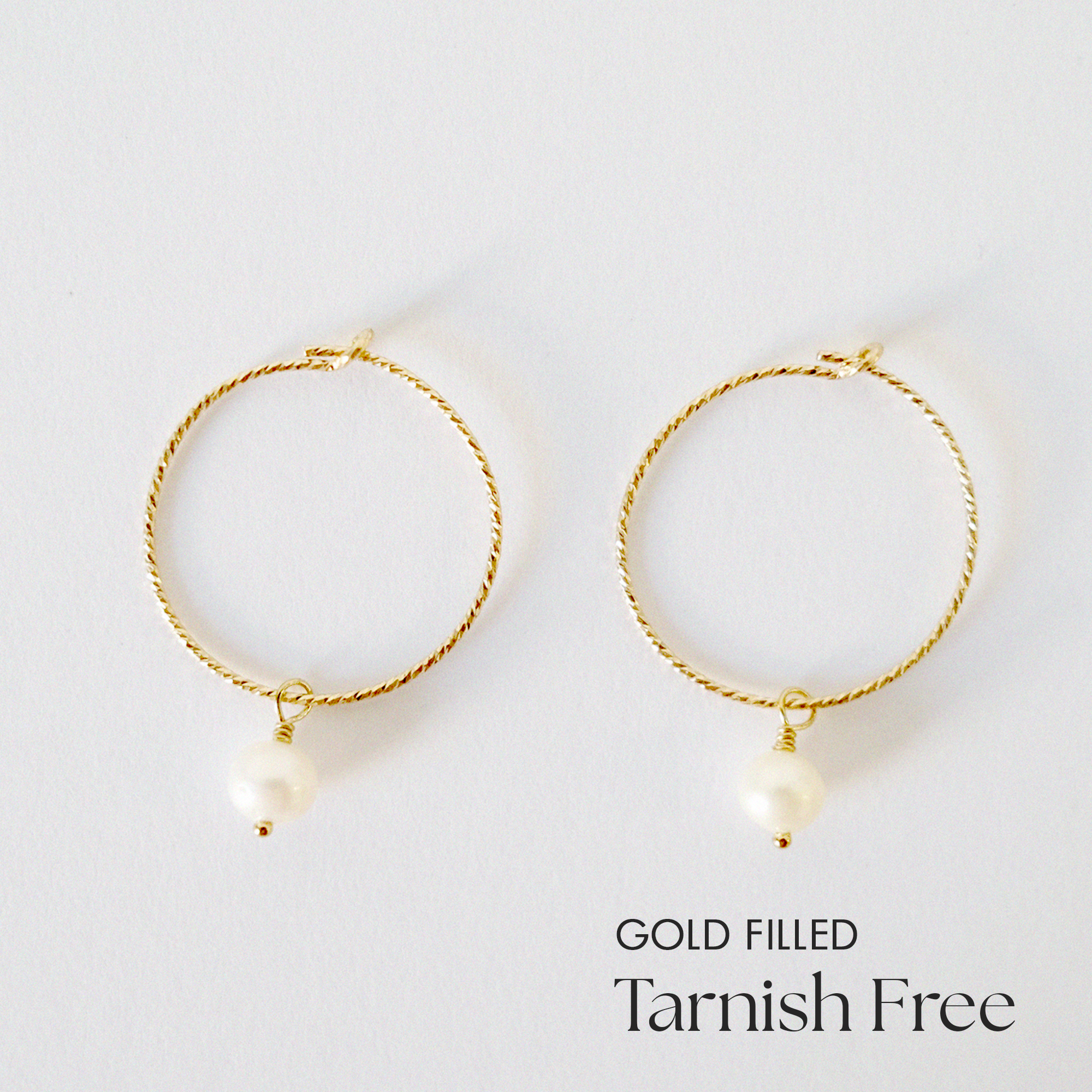 Gold-filled hoop earrings with freshwater pearl accent laid flat on white surface