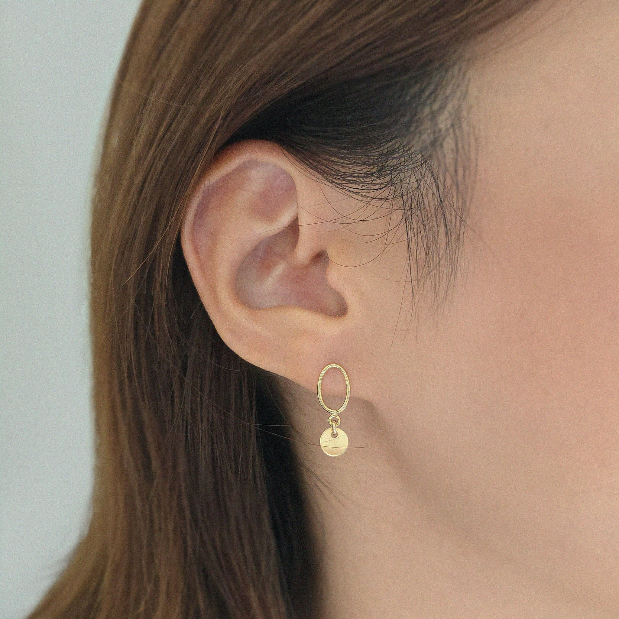 Minimal disc earrings styled on model with hair tucked behind ear