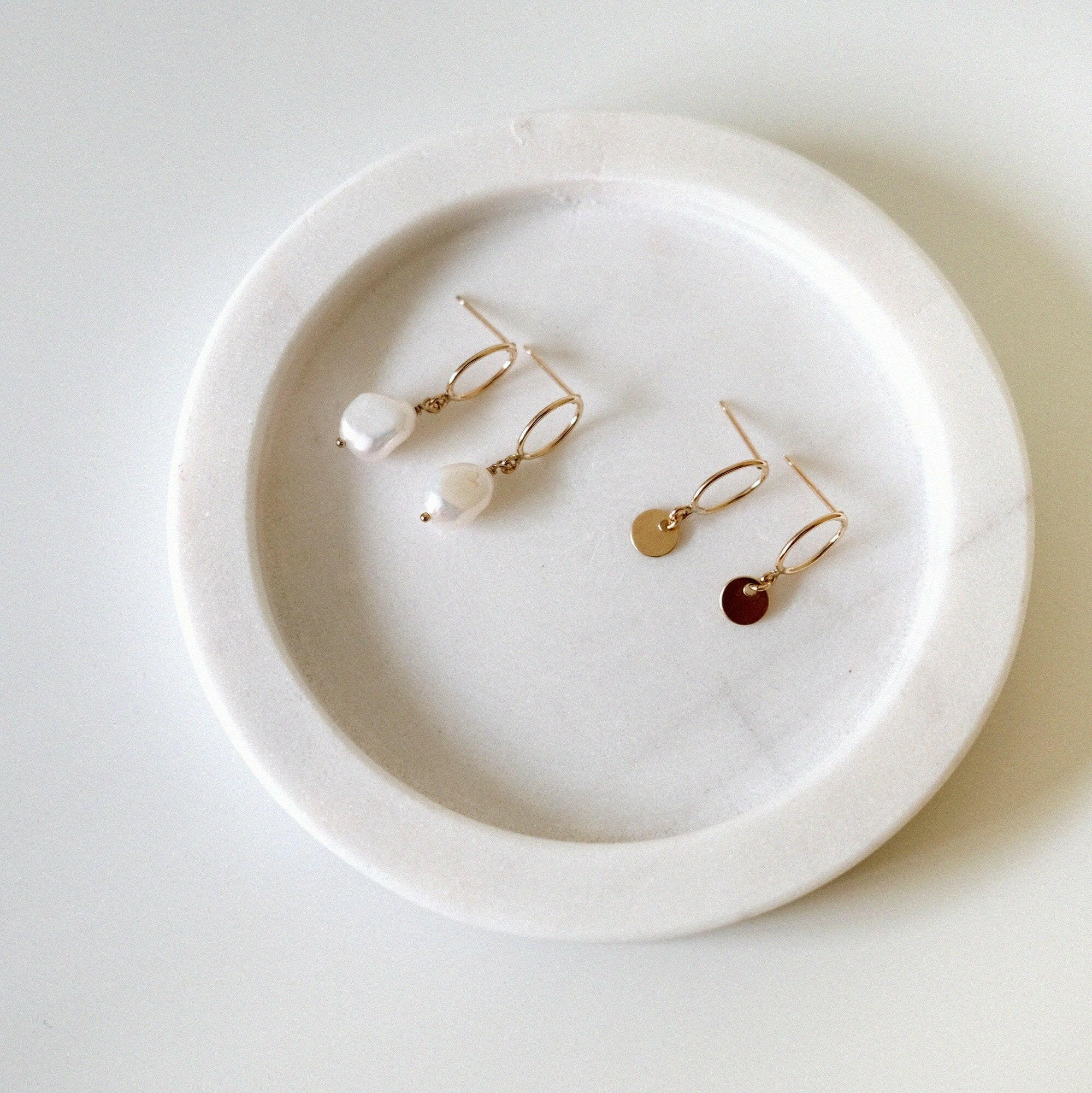 Celina Pearl and Disc Earrings displayed side by side on a soft round stone jewelry tray