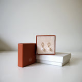 Celina Pearl Earrings displayed in a jewelry box with a minimal cream interior and brown outer packaging