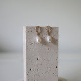 A pair of pearl drop earrings gently resting over the edge of a pink stone tray with natural texture