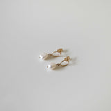 A pair of gold filled celina Pearl earrings laid flat on a surface with butterfly backs attached and facing upward