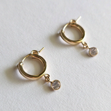 Close-up of gold filled Crystal Flex Hoop earrings with dangling cubic zirconia accents on white background