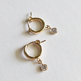 Gold filled hoop earrings featuring small round cubic stones, styled simply on textured white surface