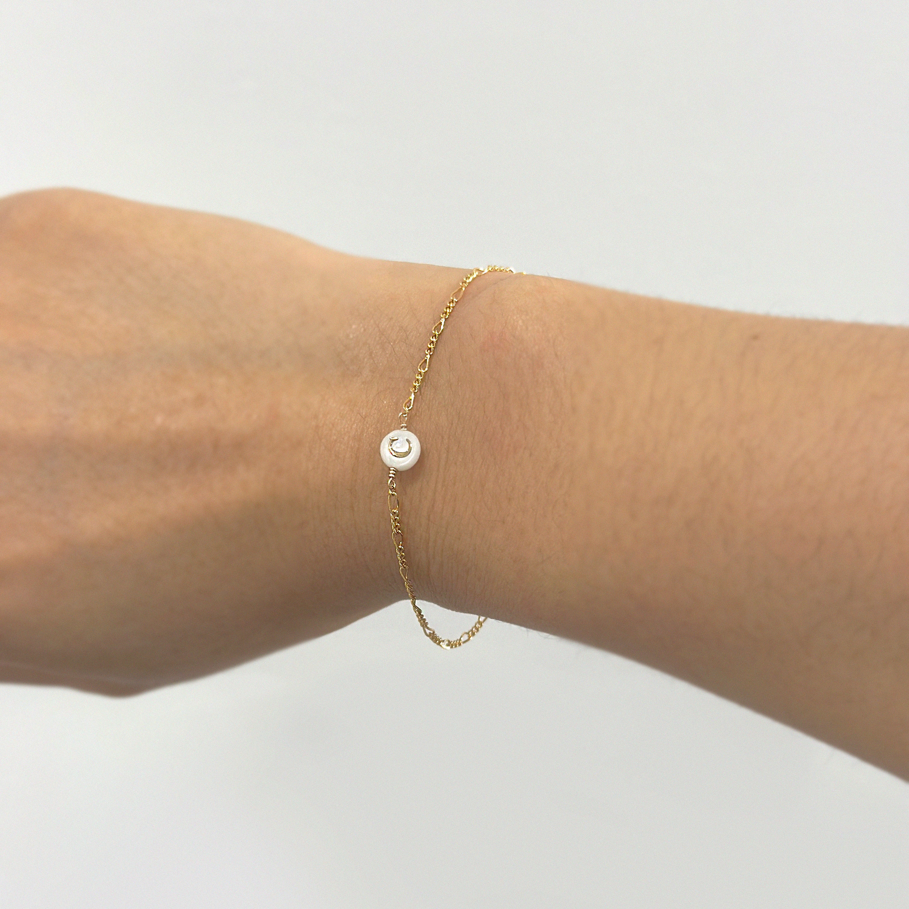 Gold bracelet with a mother of pearl initial charm on a wrist against a white background