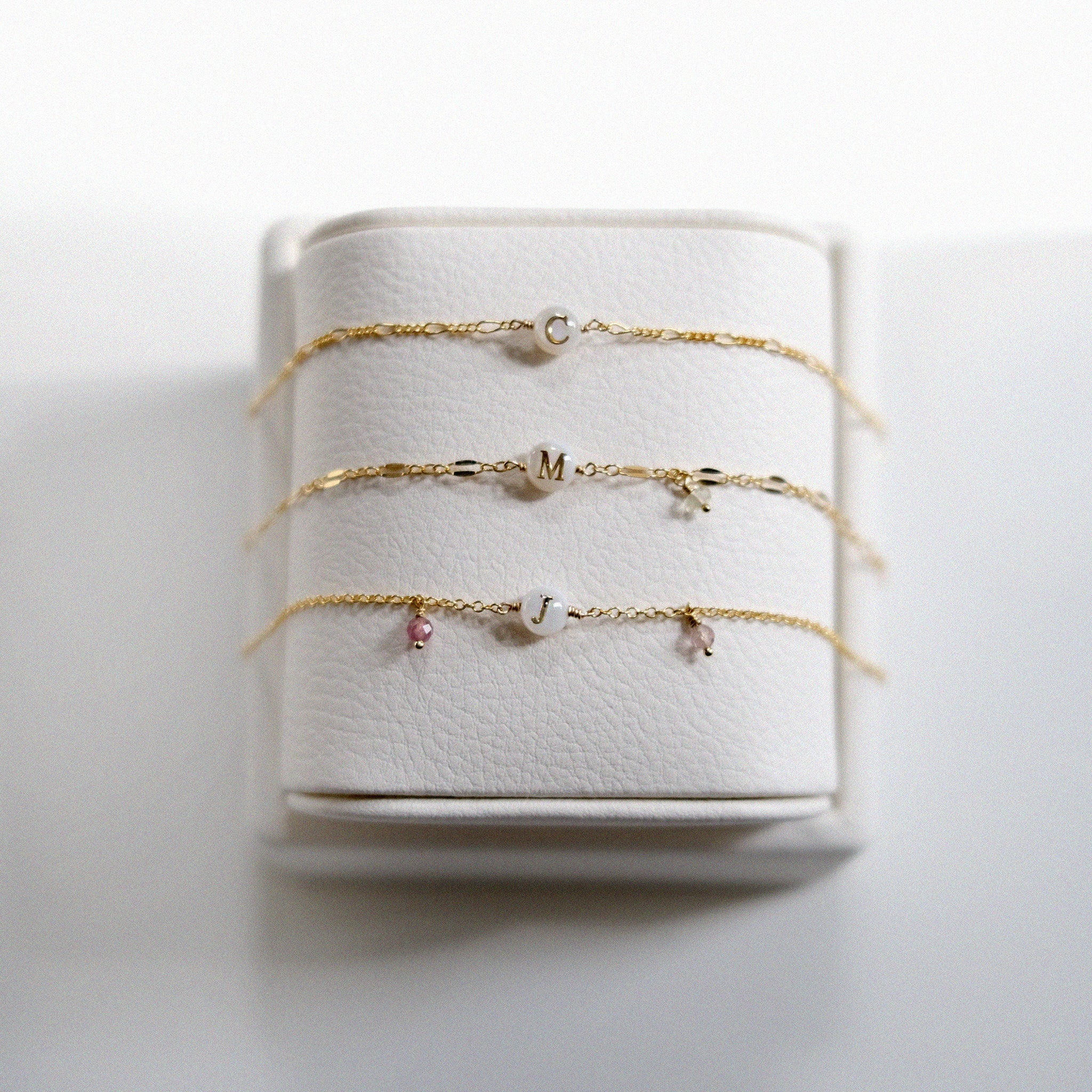 Set of gold filled custom bracelets with small charms on a white bracelet holder
