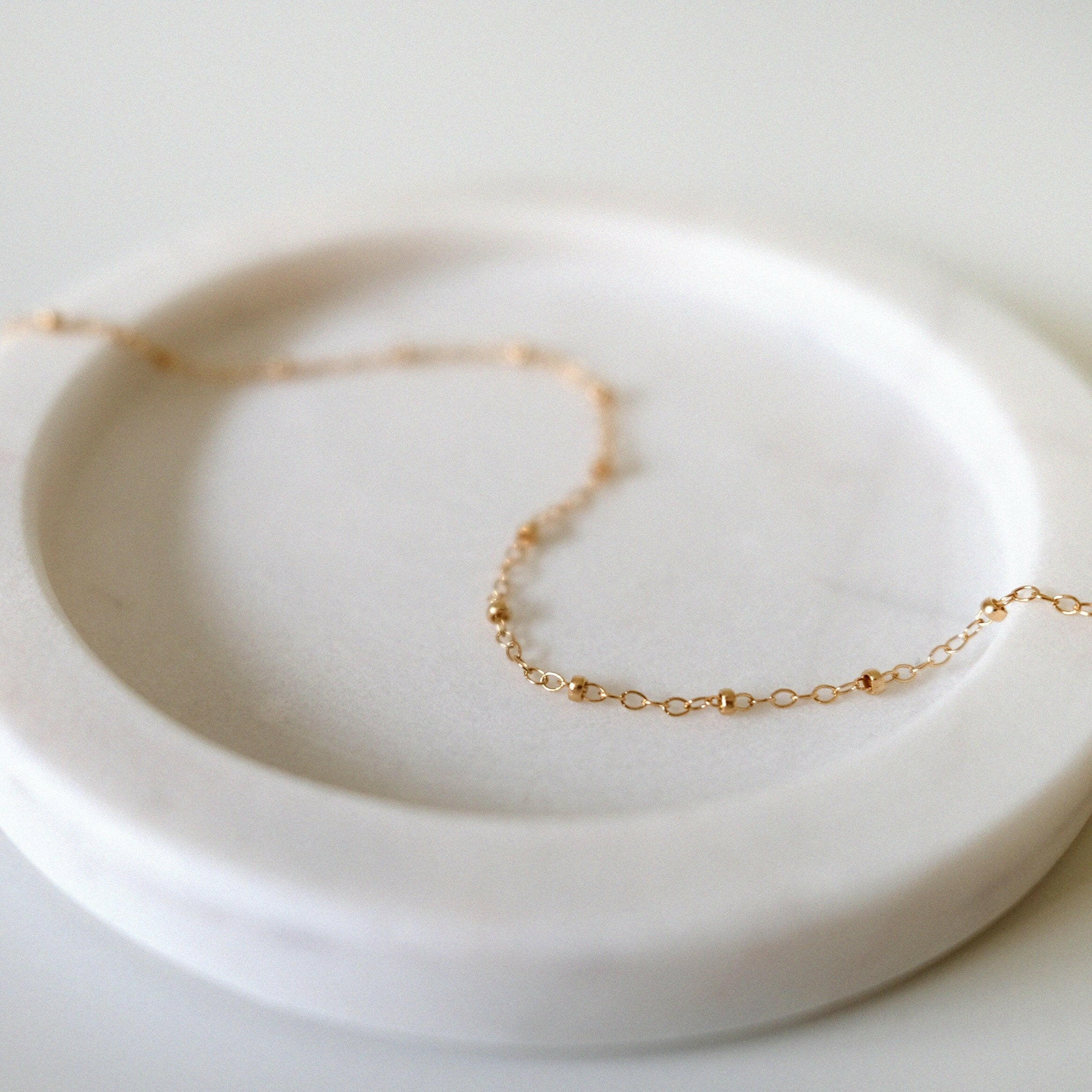 Dotty Chain II Anklet styled on a soft light pink tray, highlighting delicate gold bead accents