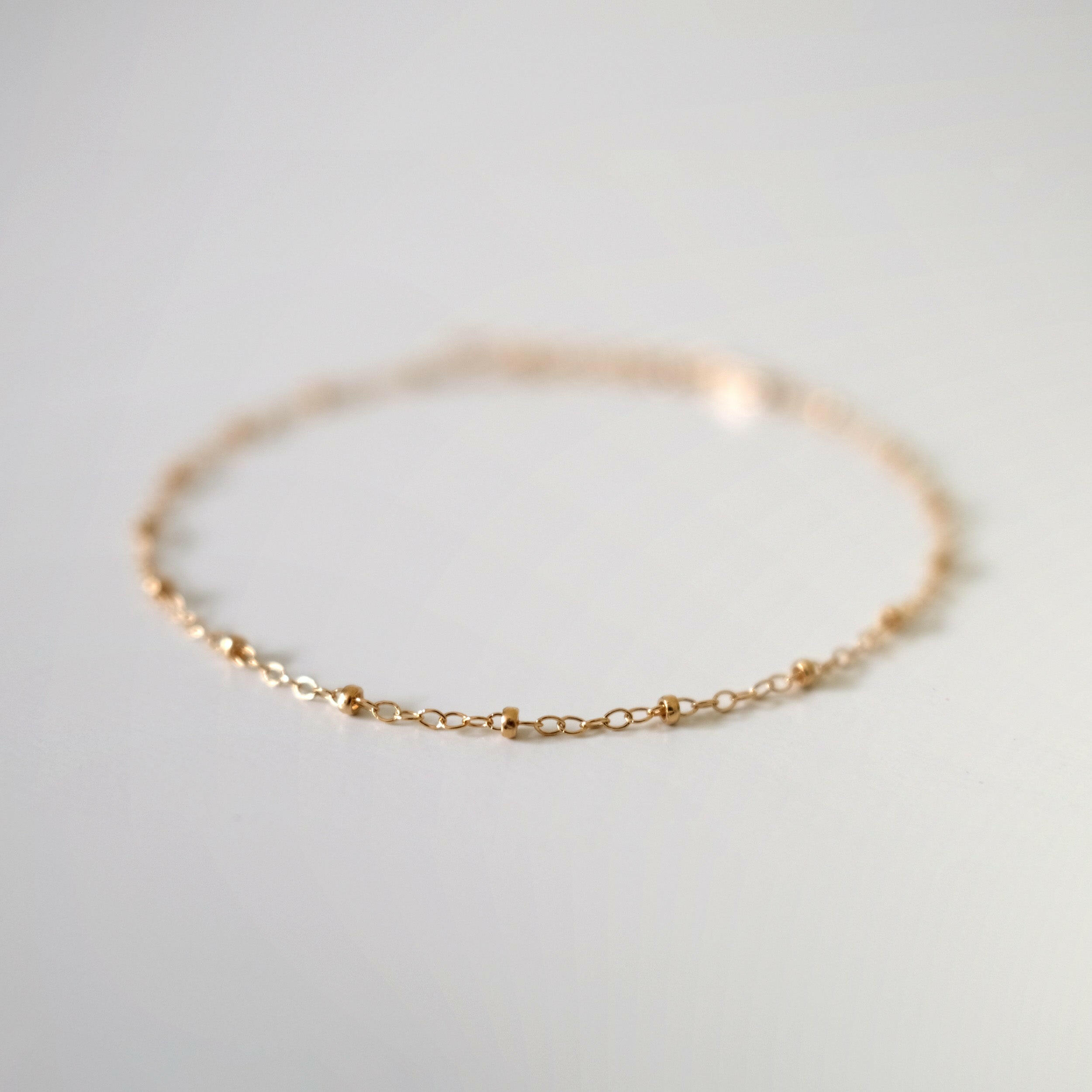 Macro shot focusing on front section of anklet chain with gold beads in sharp detail, background softly blurred