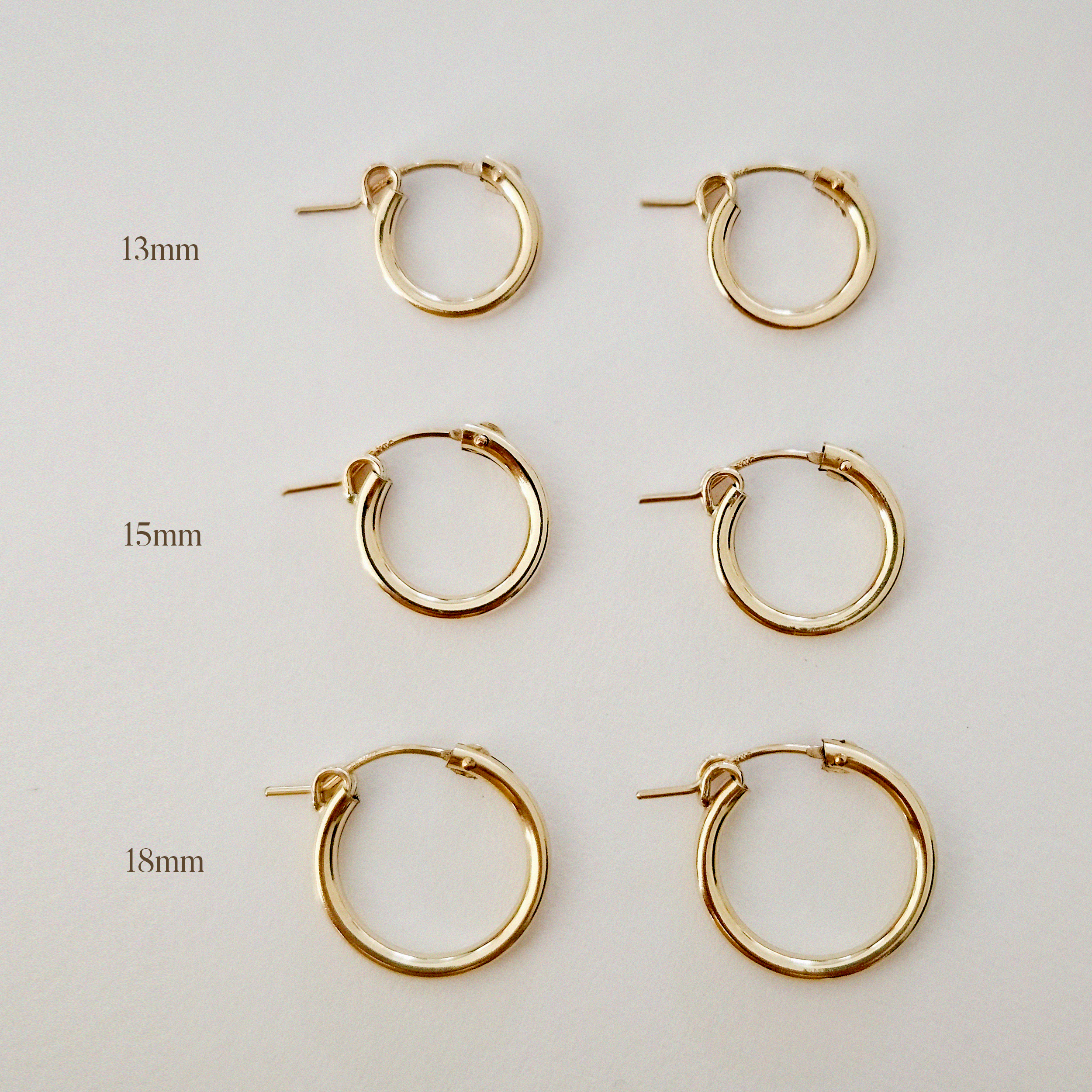 Set of 13mm, 15mm, and 18mm gold-filled hoop earrings displayed flat on white background.