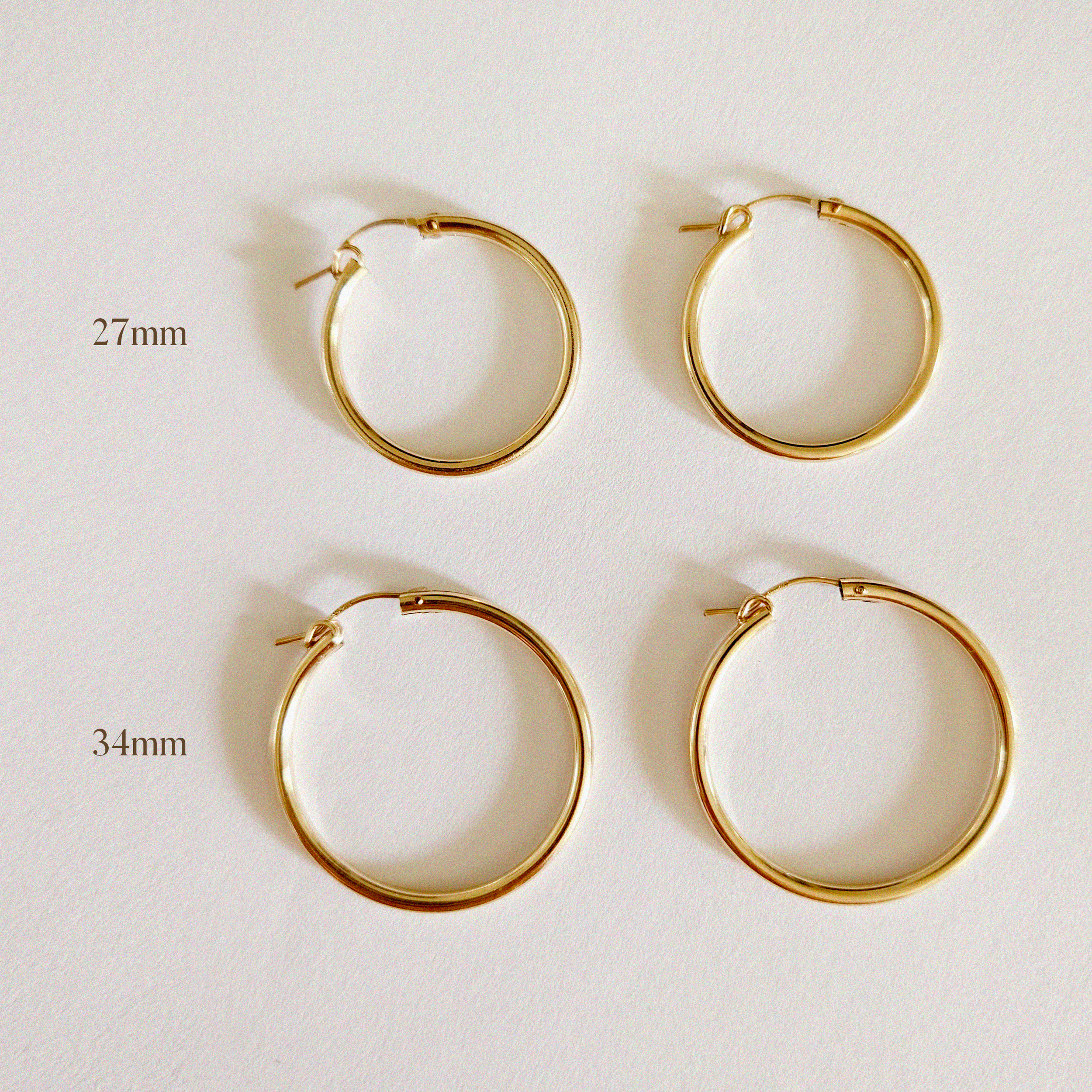 Pair of 27mm and 34mm gold-filled hoop earrings laid flat on white background