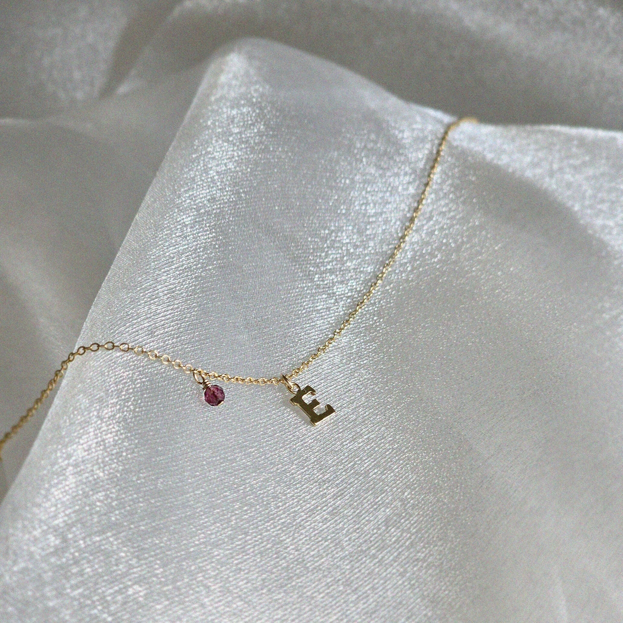 Gold Filled Initial Necklace with birthstone placed on shimmery fabric