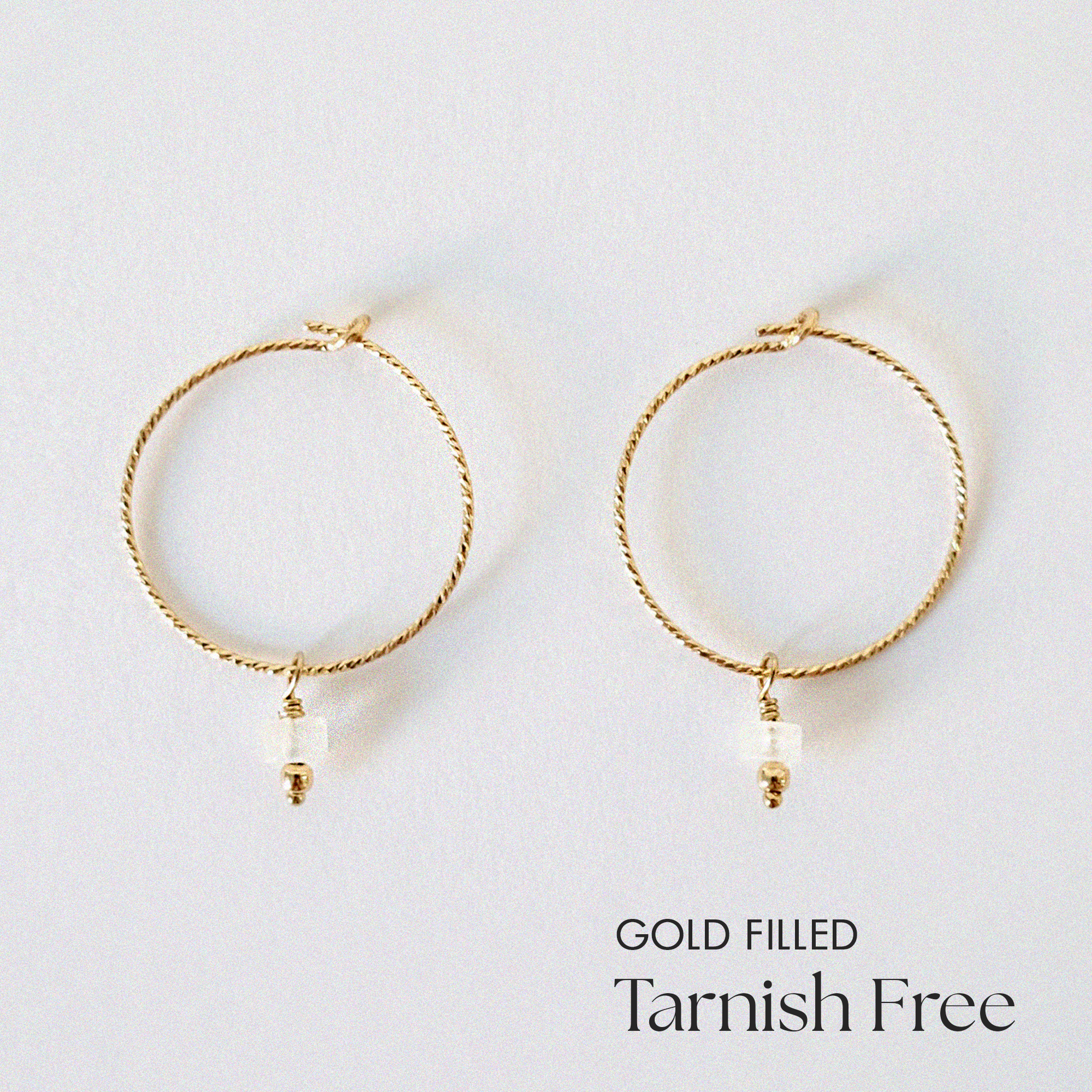 Gold-filled hoop earrings with natural moonstone charms laid flat on a white background