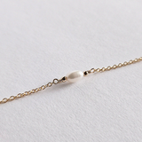 Macro shot of gold chain links connecting to oval shaped pearl