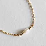 Gold filled chain structure in sharp focus alongside pearl
