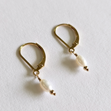 Close-up side view of gold hook and hanging pearl in soft light